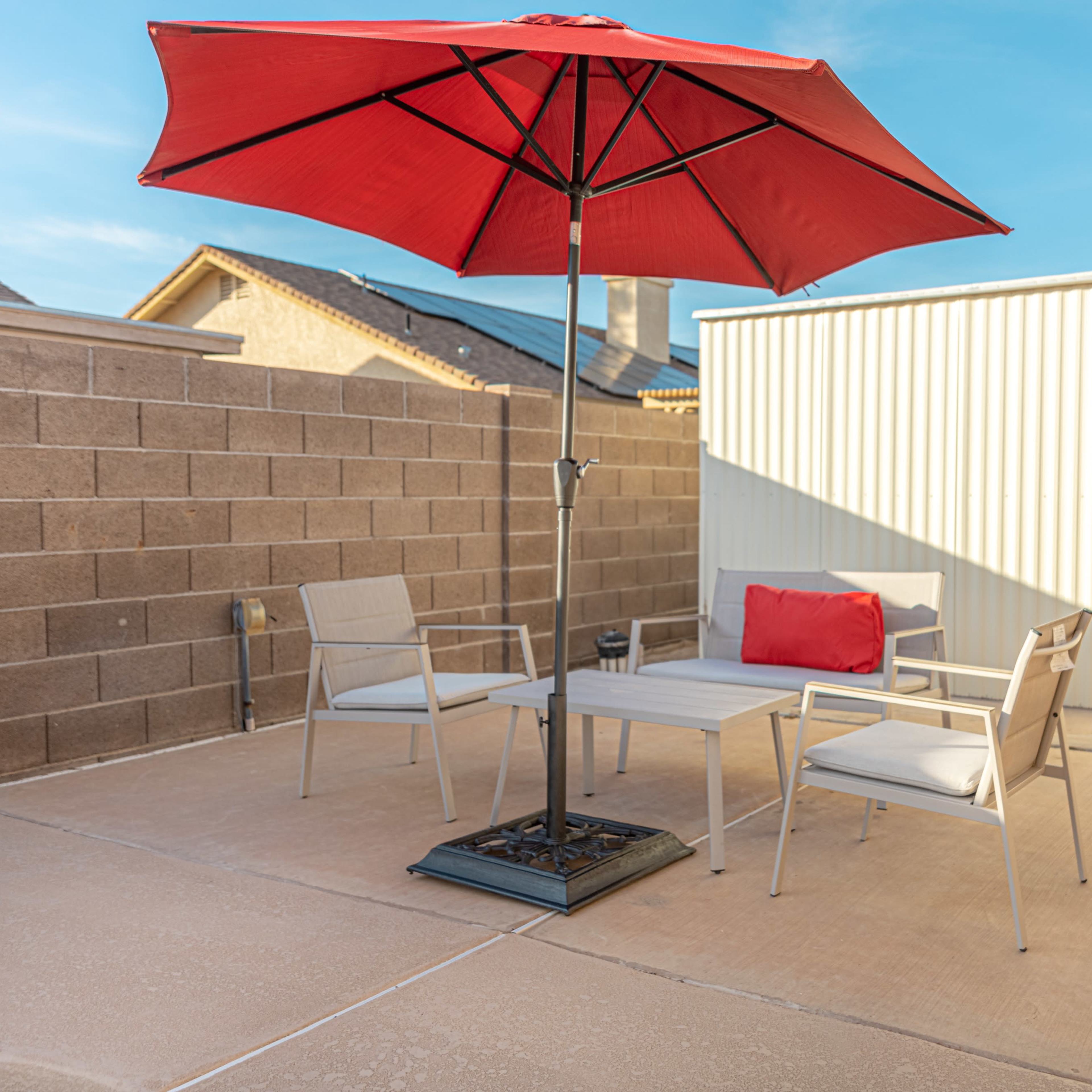 A red umbrella shades a small outdoor seating area with two chairs and a table on a concrete patio surrounded by a brick wall.