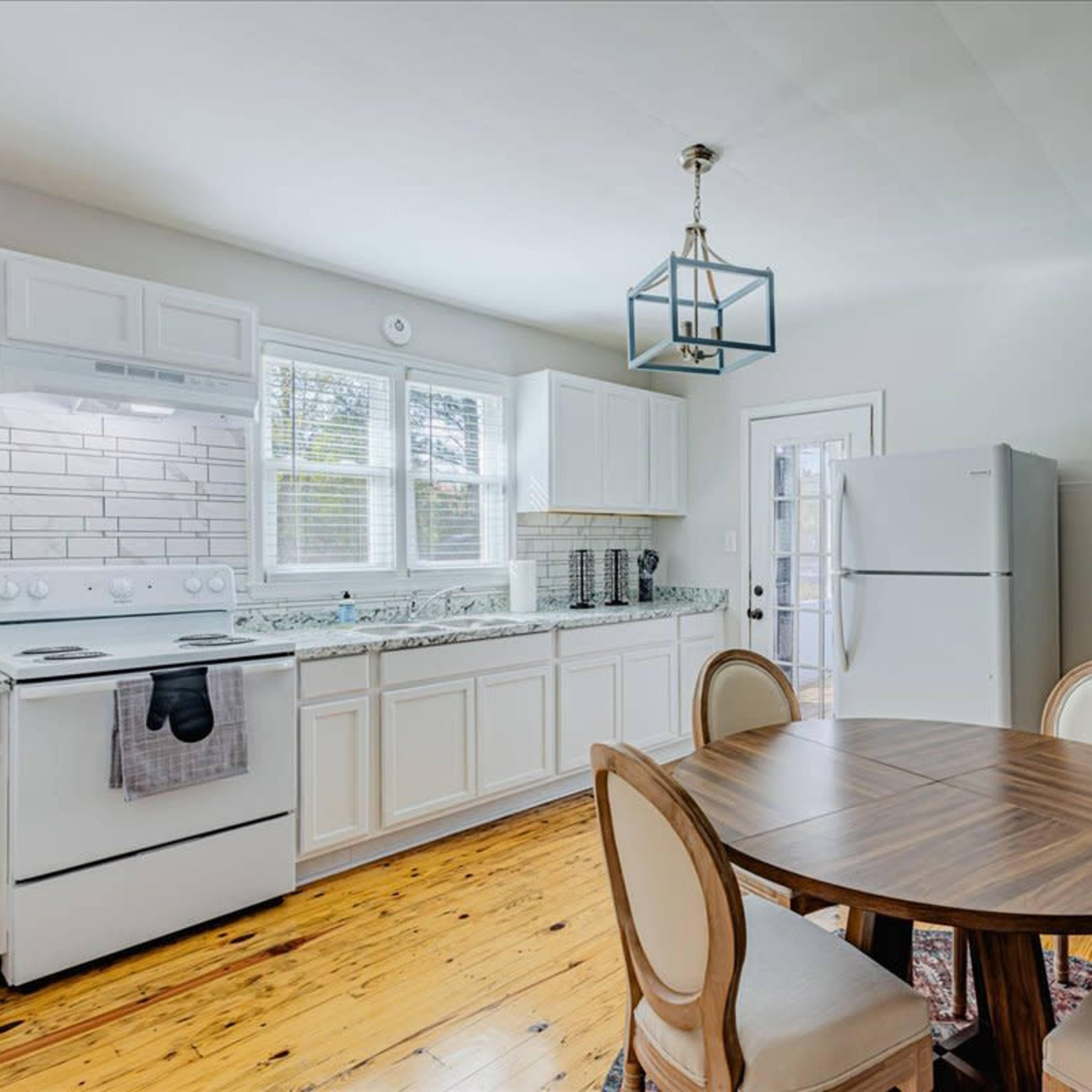 A modern kitchen features white cabinets, a tile backsplash, and a round dining table with four chairs.