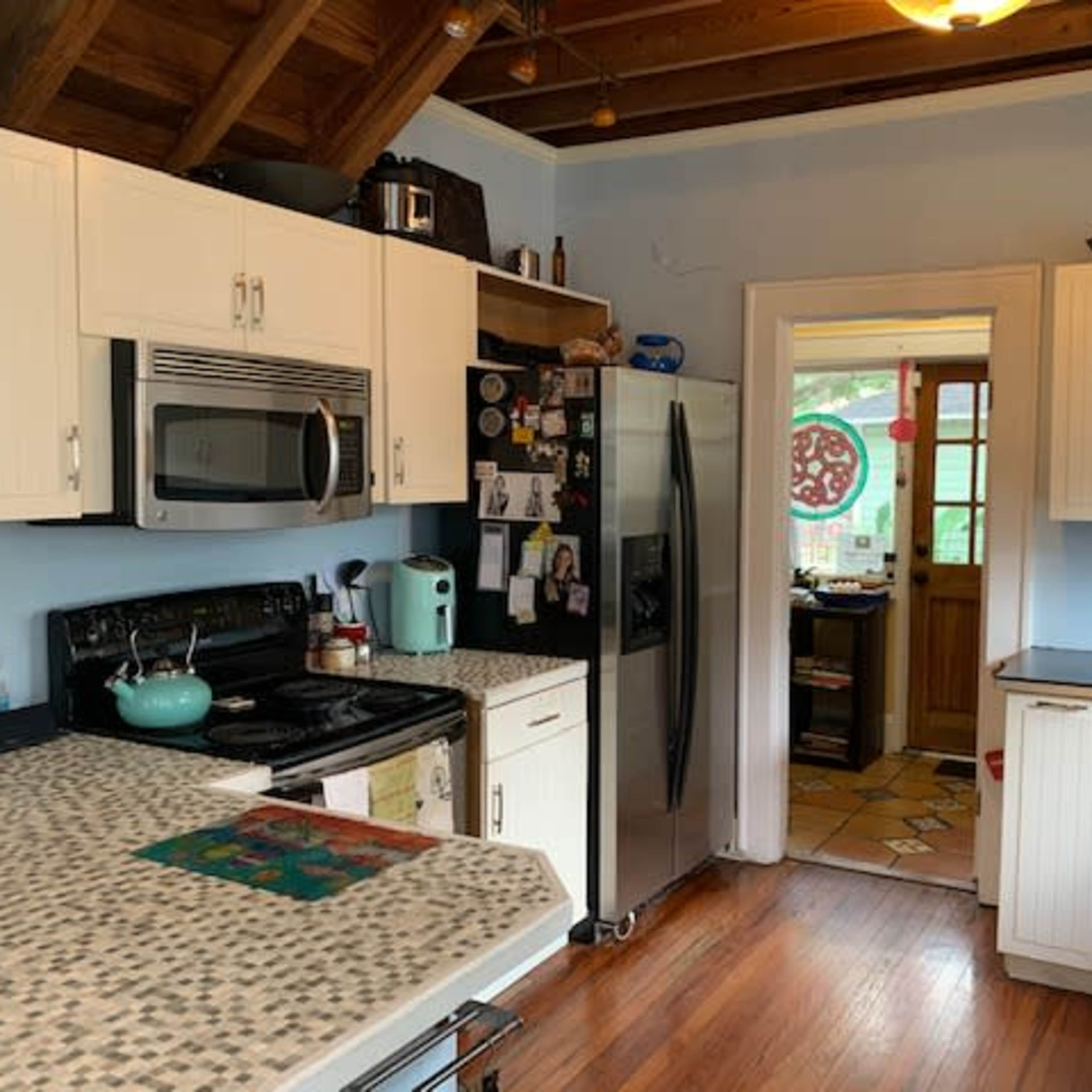 A kitchen with white cabinets, a stainless steel refrigerator, and a wooden floor, featuring a large counter with a mosaic design.