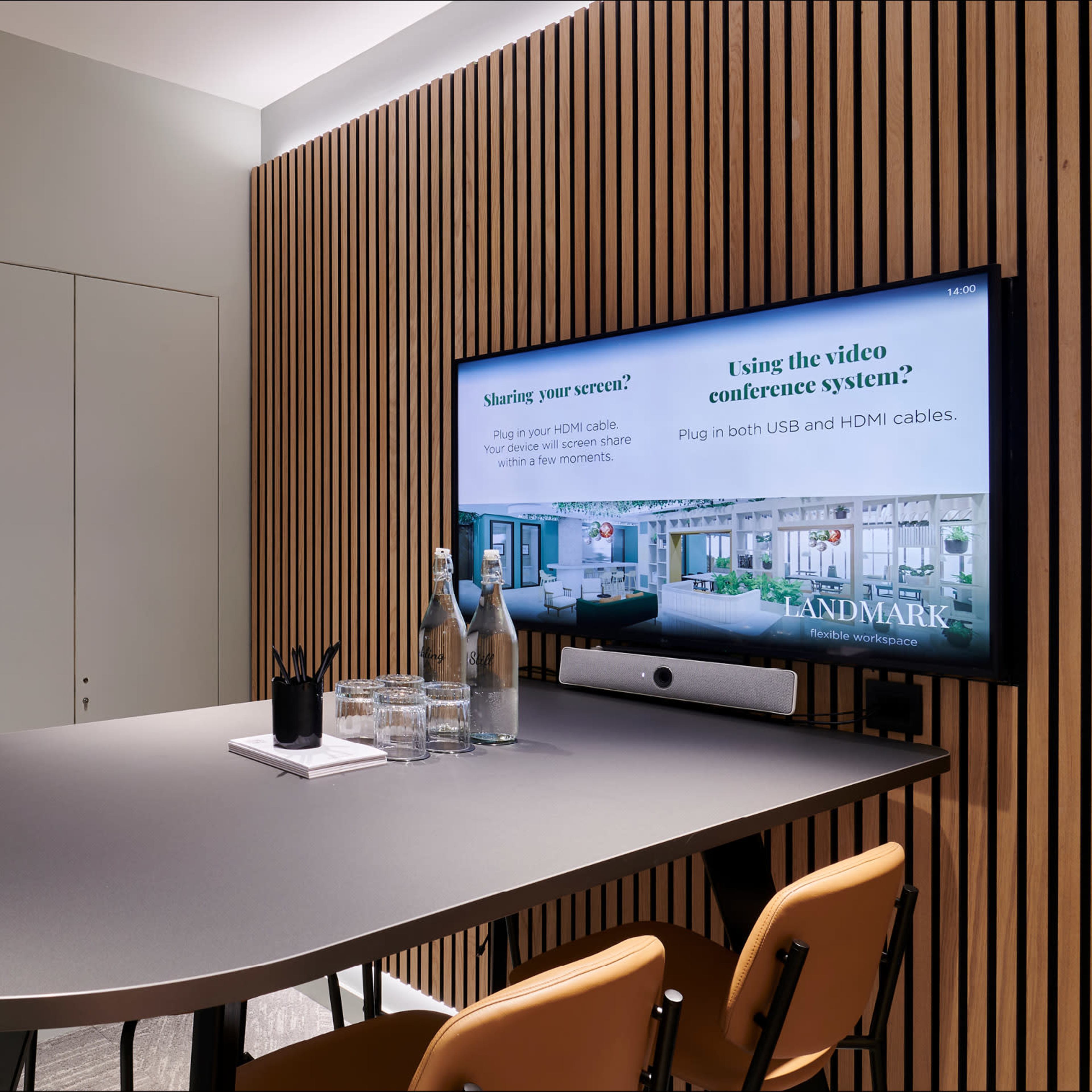 A meeting room features a large table, a television displaying instructions for video conferencing, and a backdrop of wooden paneling.