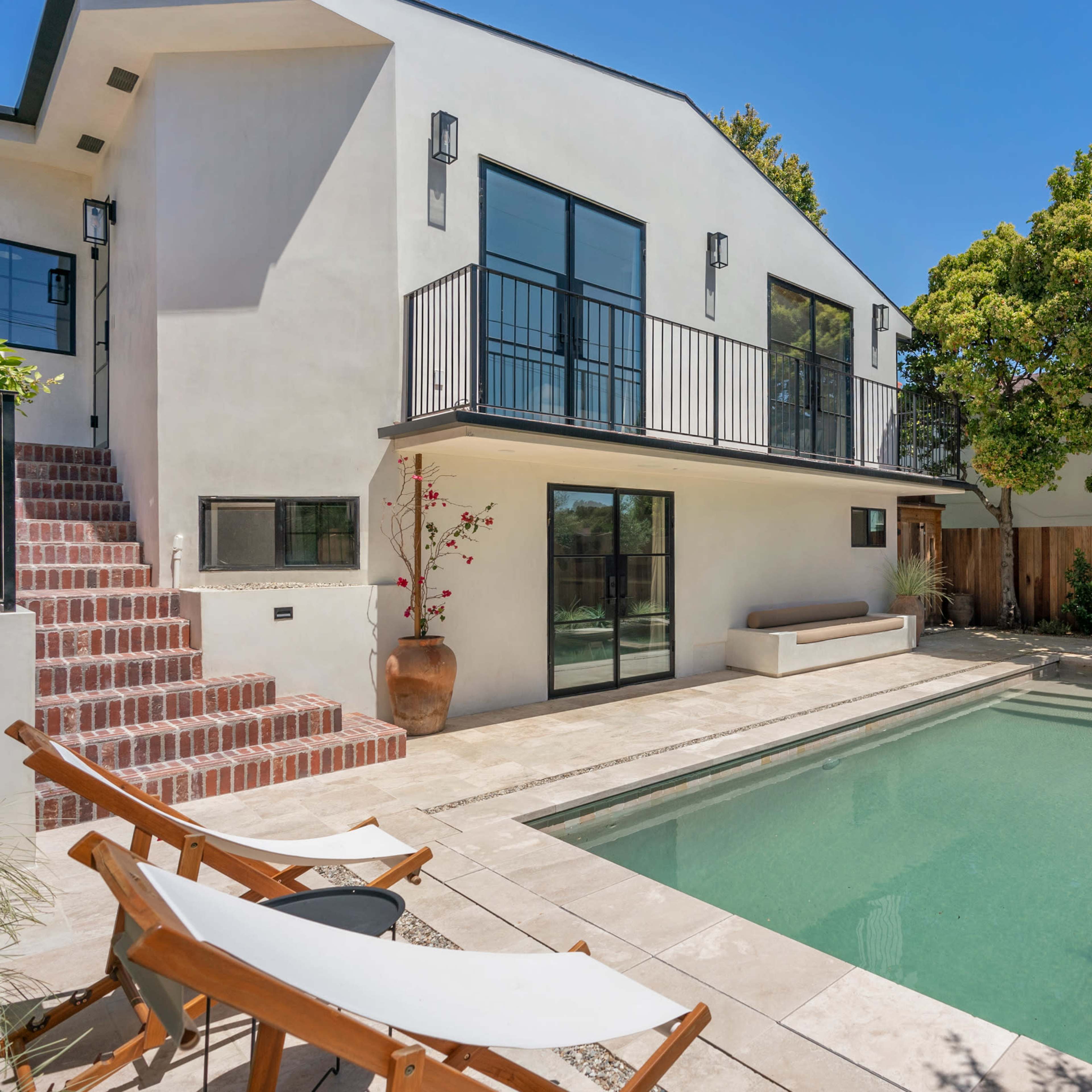 A modern two-story house with a swimming pool and several lounge chairs in a landscaped backyard.