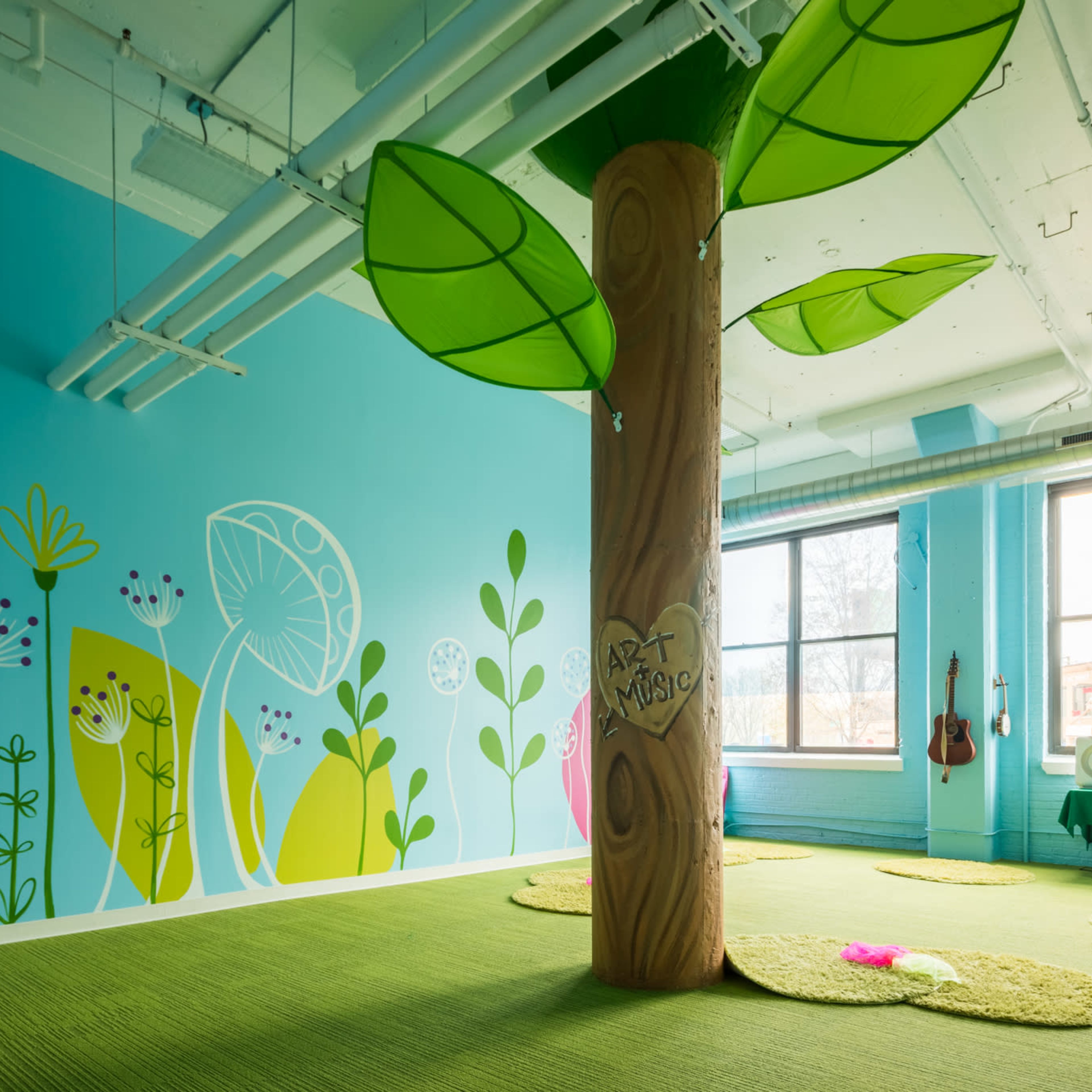 A brightly colored playroom featuring a large tree structure with green leaves and a mural of flowers and plants on the walls.