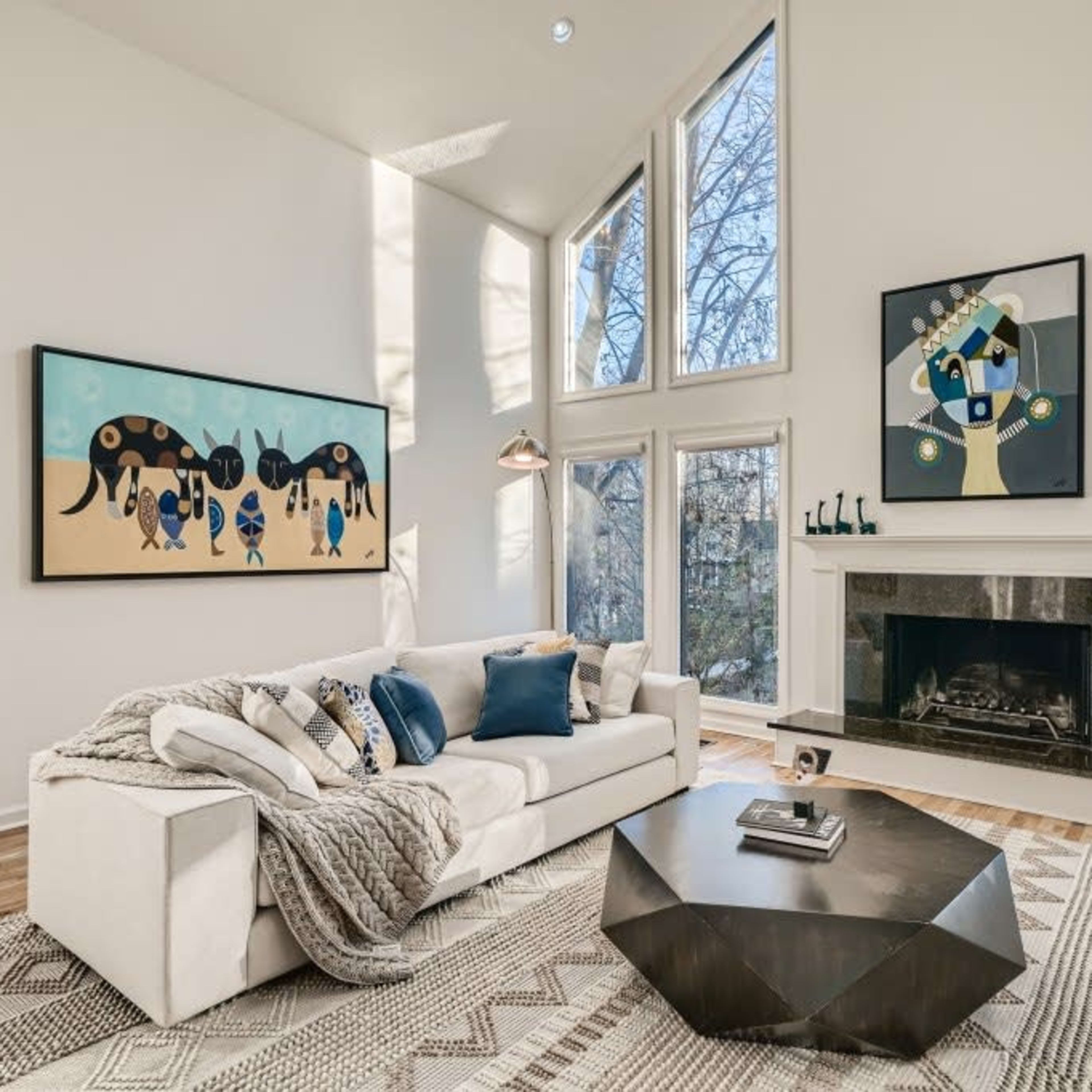 A bright living room features large windows, a modern fireplace, and contemporary artwork on the walls.