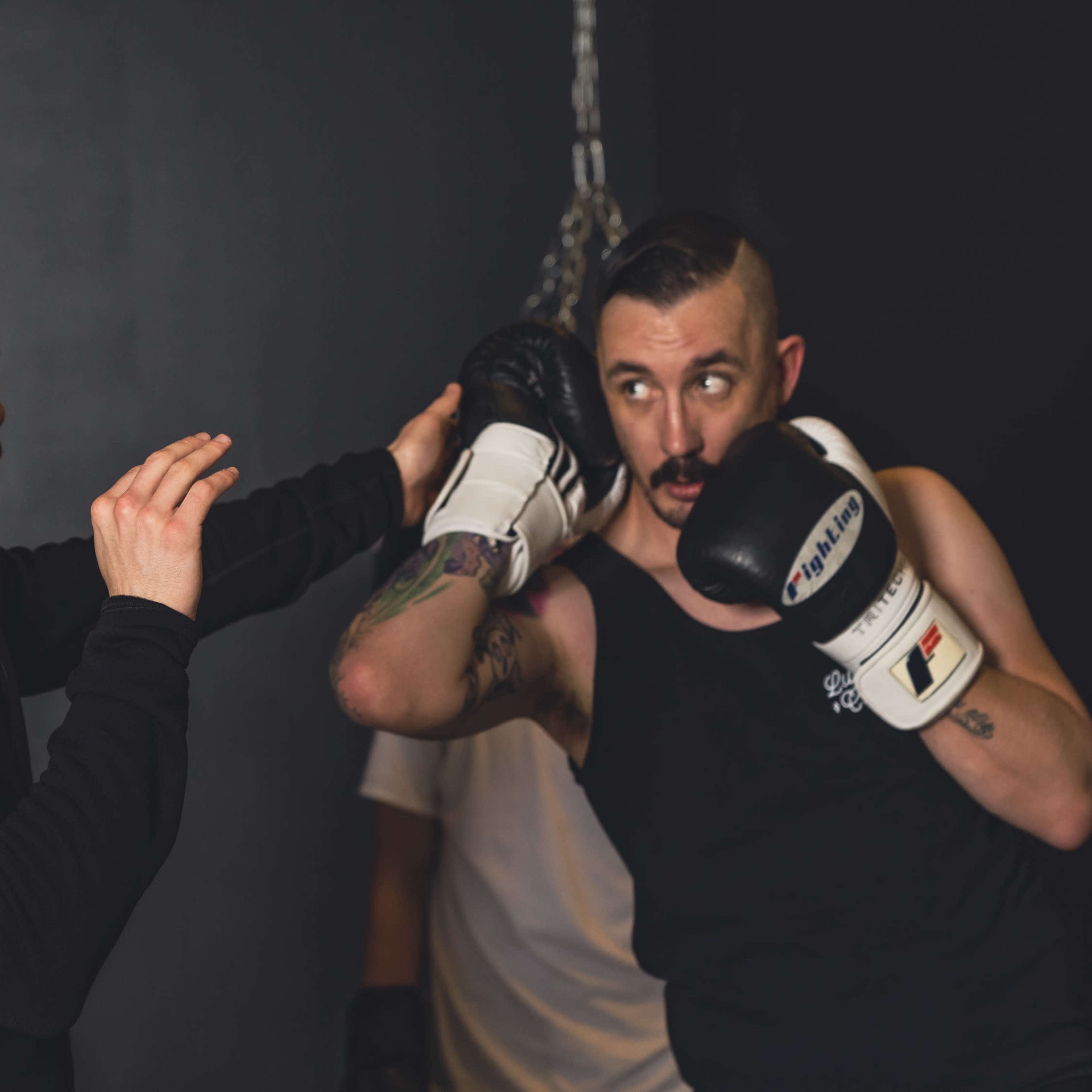 Two men are sparring in a boxing gym, with one man throwing a punch while the other protects himself with gloves.