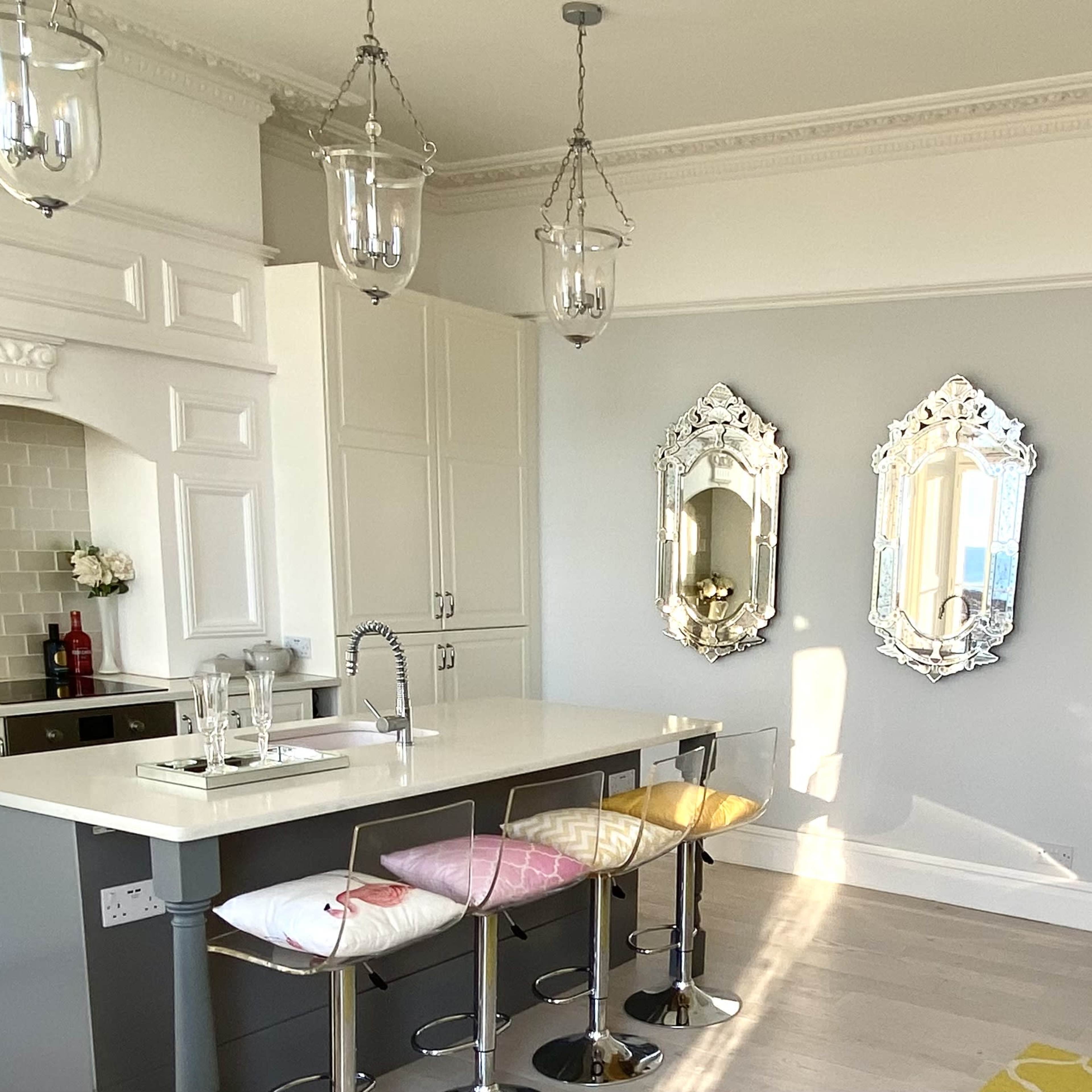 A modern kitchen with a central island, three bar stools, and three decorative mirrors on a light gray wall.
