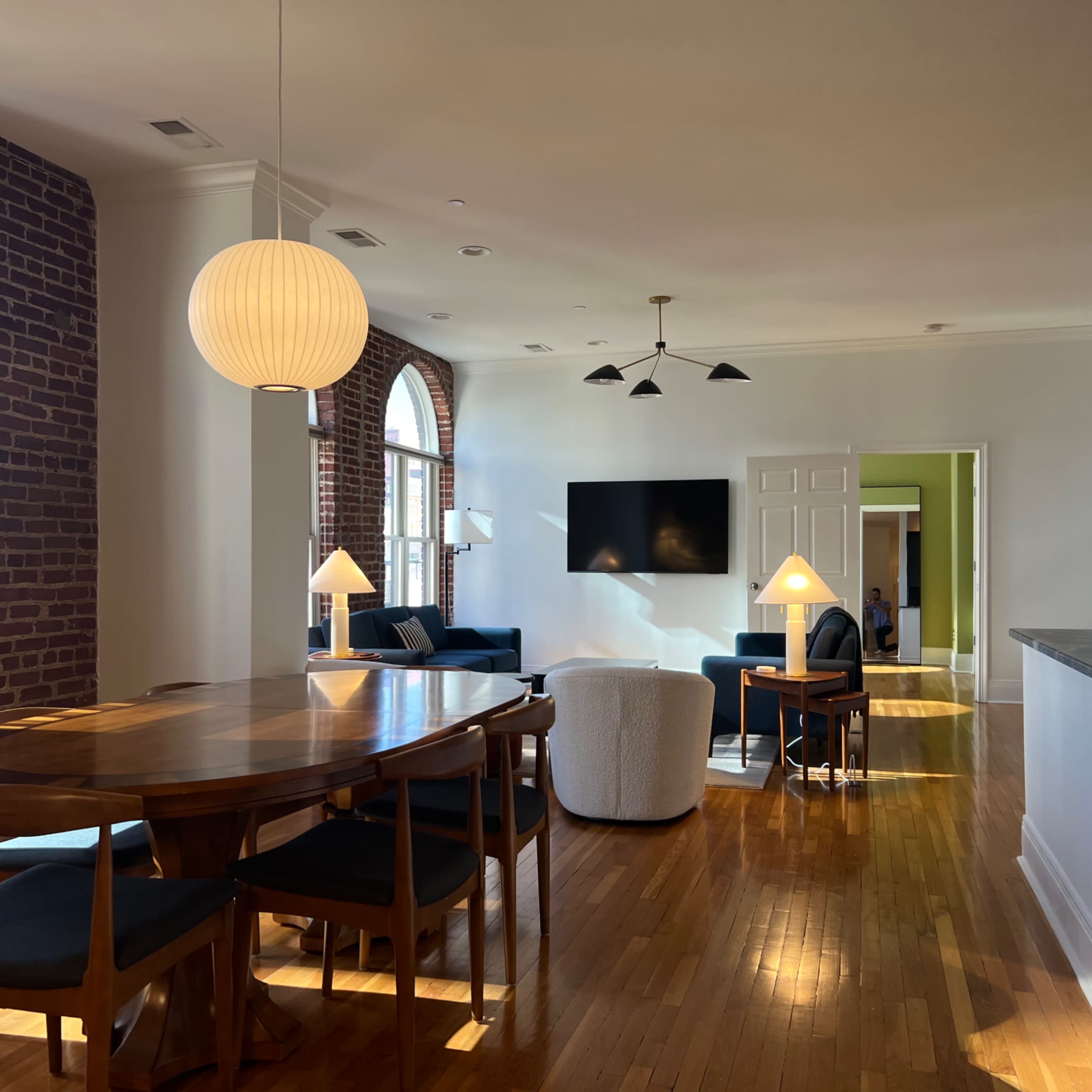 A spacious living area with a dining table, a seating area featuring a sofa and chairs, and large windows allowing natural light to illuminate the room.