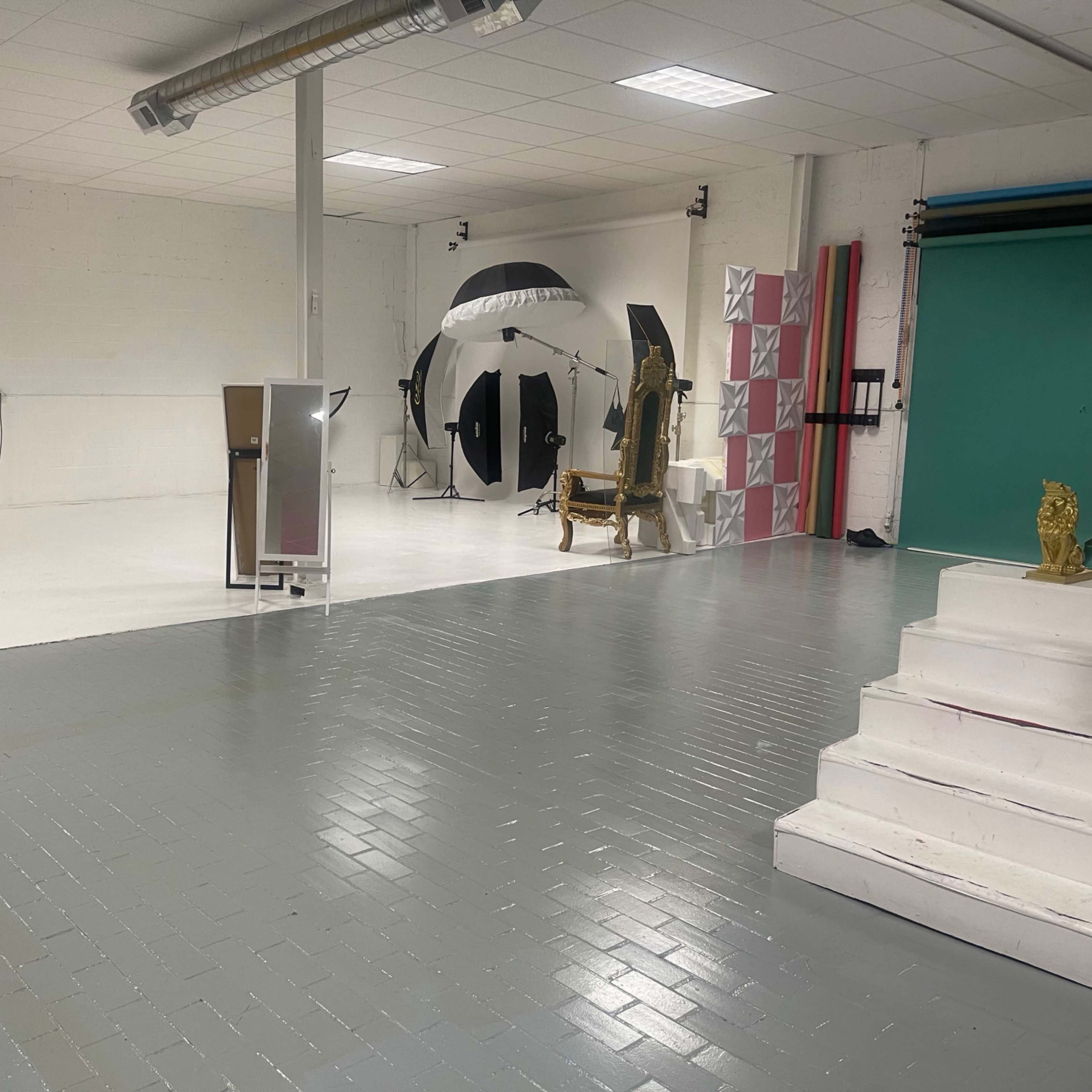 A photography studio featuring a white floor, various lighting equipment, and backdrops in black and green.