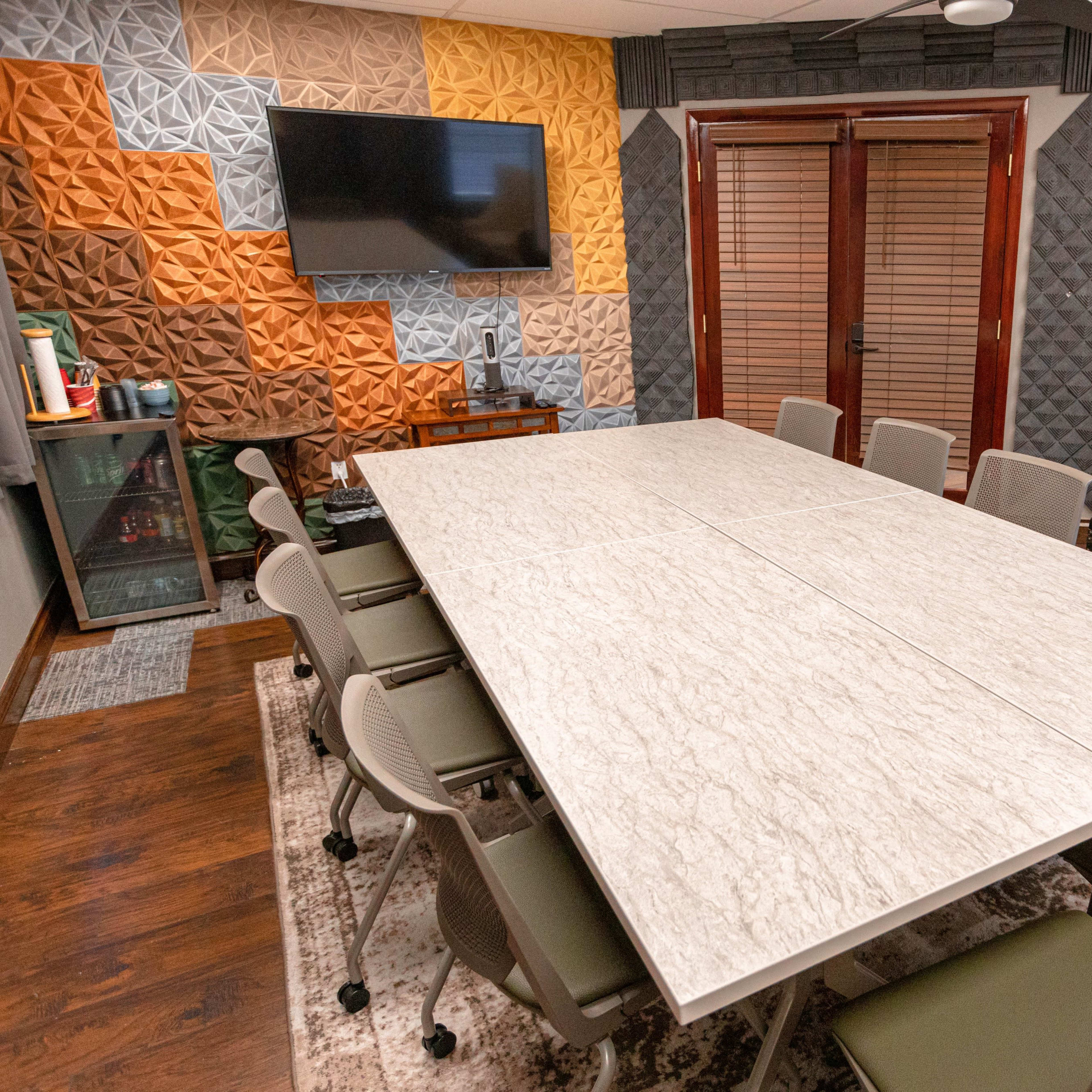 A modern conference room with a large table surrounded by chairs, and walls featuring textured acoustic panels and a television mounted on one side.
