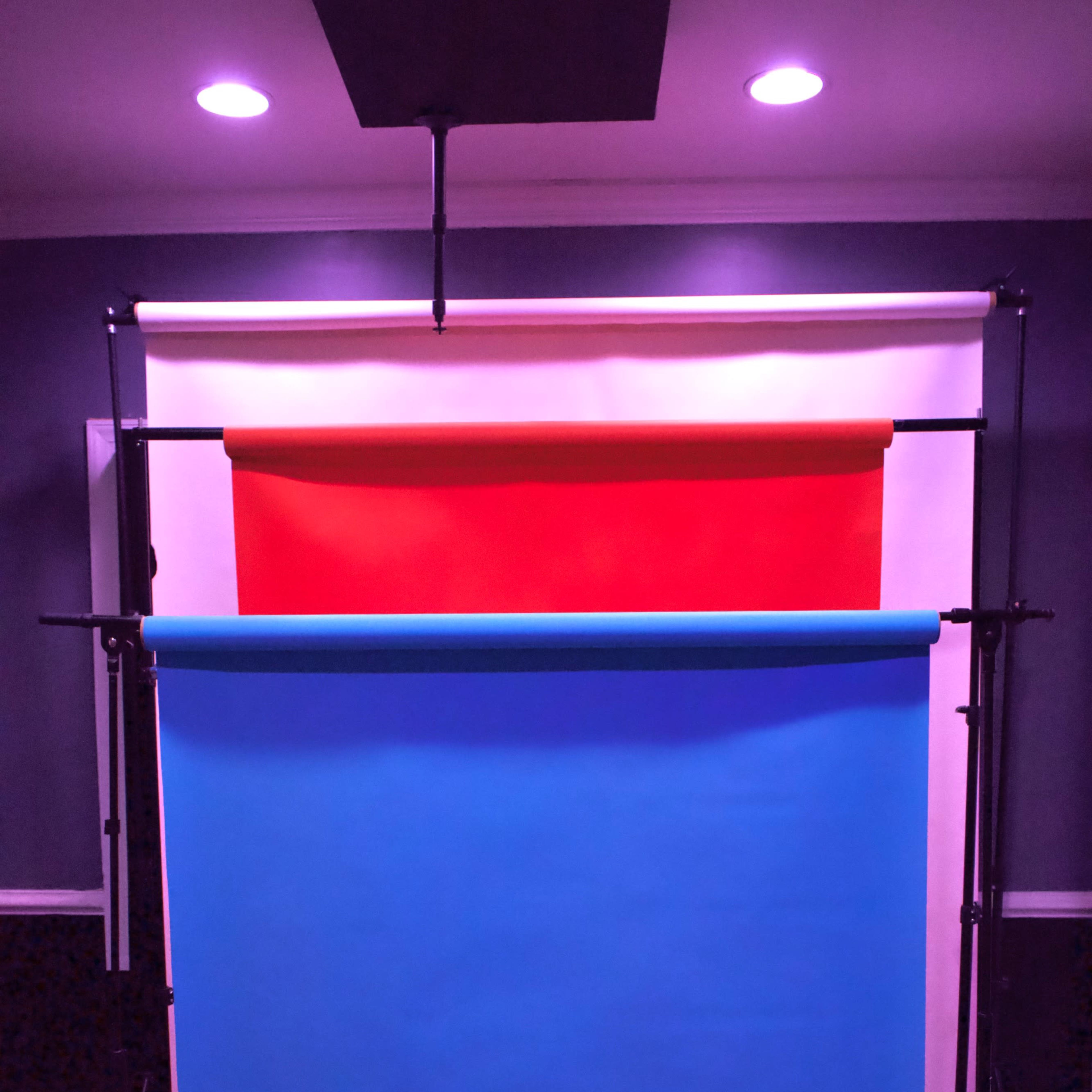 Three backdrop paper rolls in red, white, and blue, mounted on stands in a studio setting.