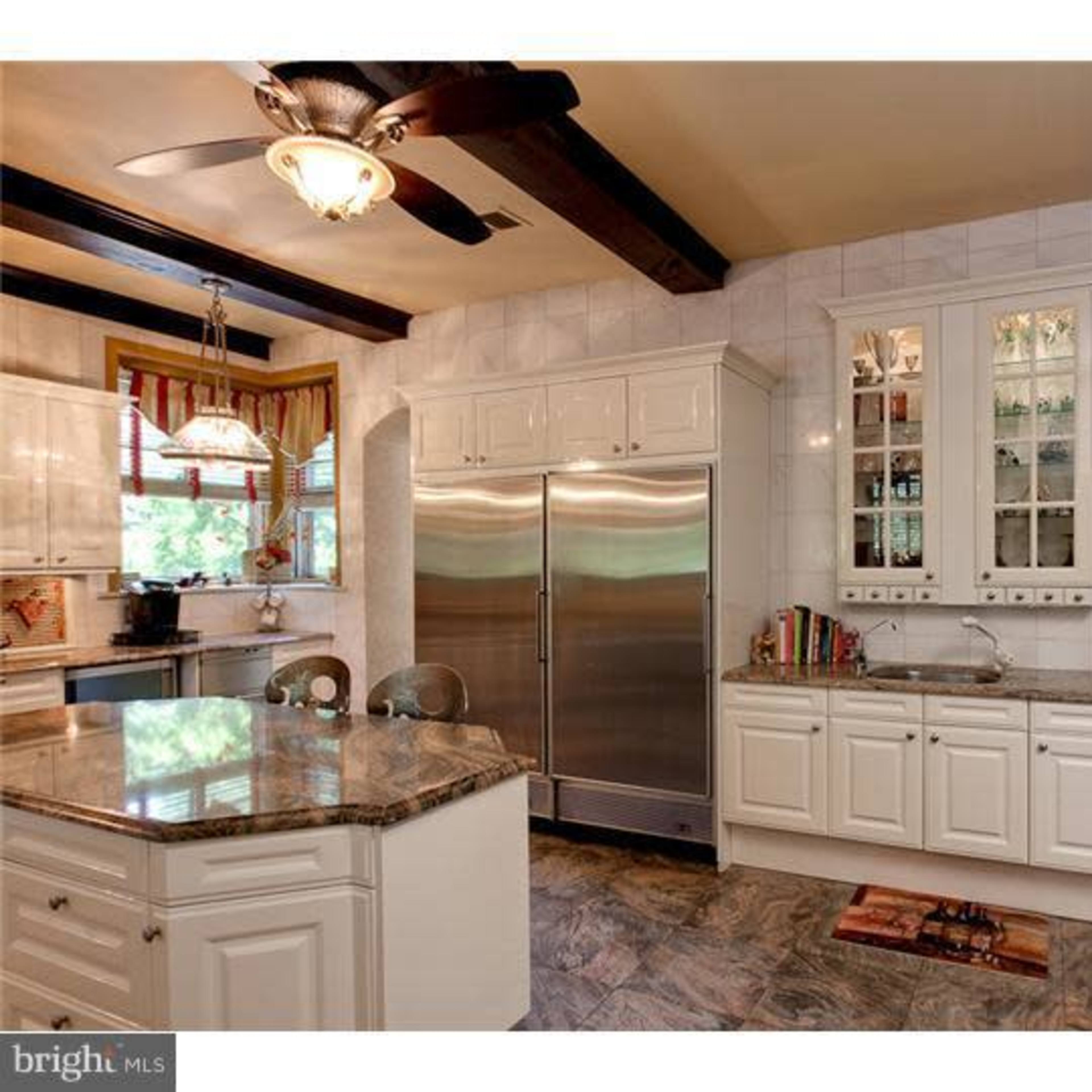 A modern kitchen with white cabinetry, a large stainless steel refrigerator, and a granite countertop.