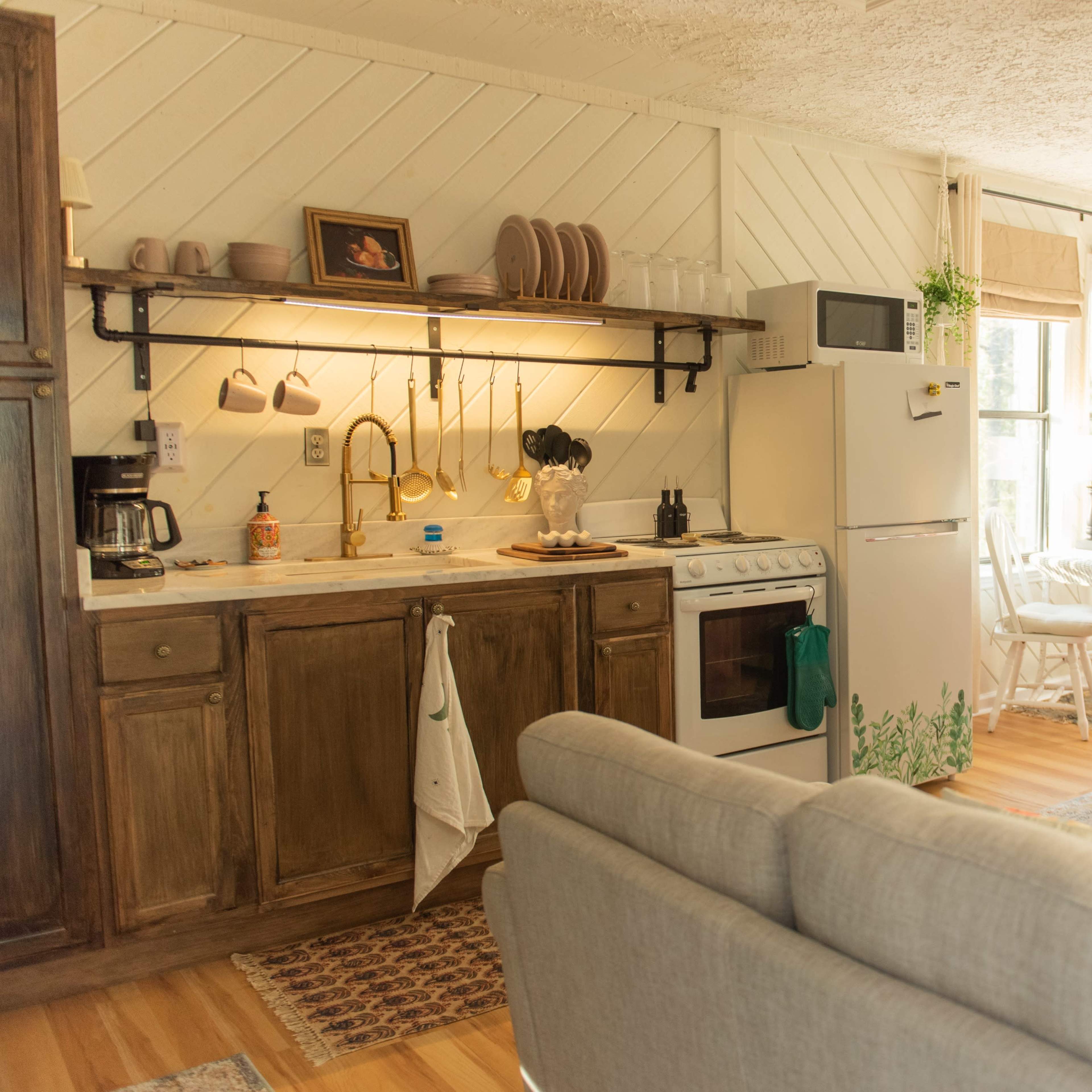A cozy kitchen features a stove, fridge, sink, and countertop adorned with kitchenware, alongside a living area with a sofa and coffee table.