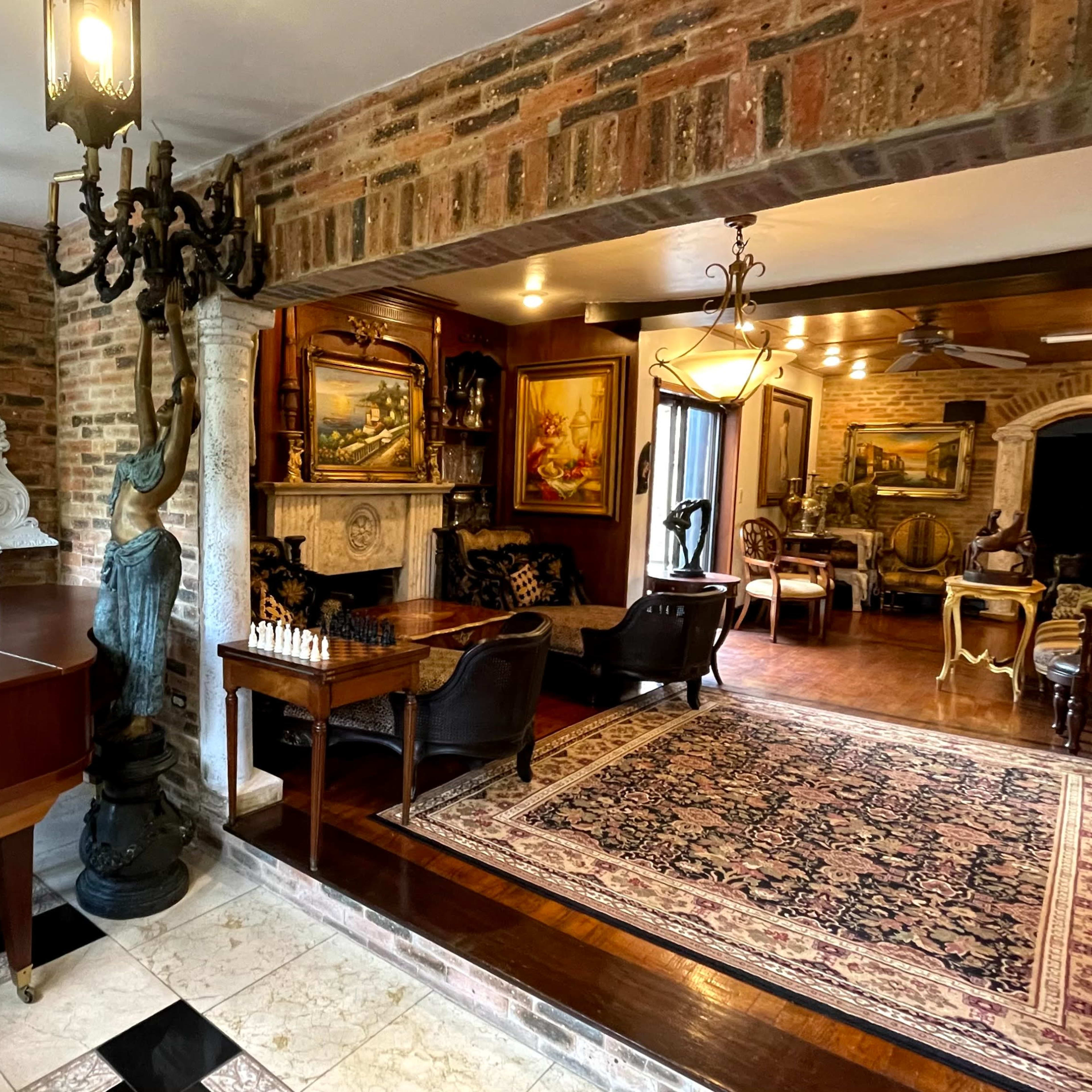 An elegantly furnished room featuring a grand piano, ornate mirror, and various seating areas with decorative paintings on the walls.