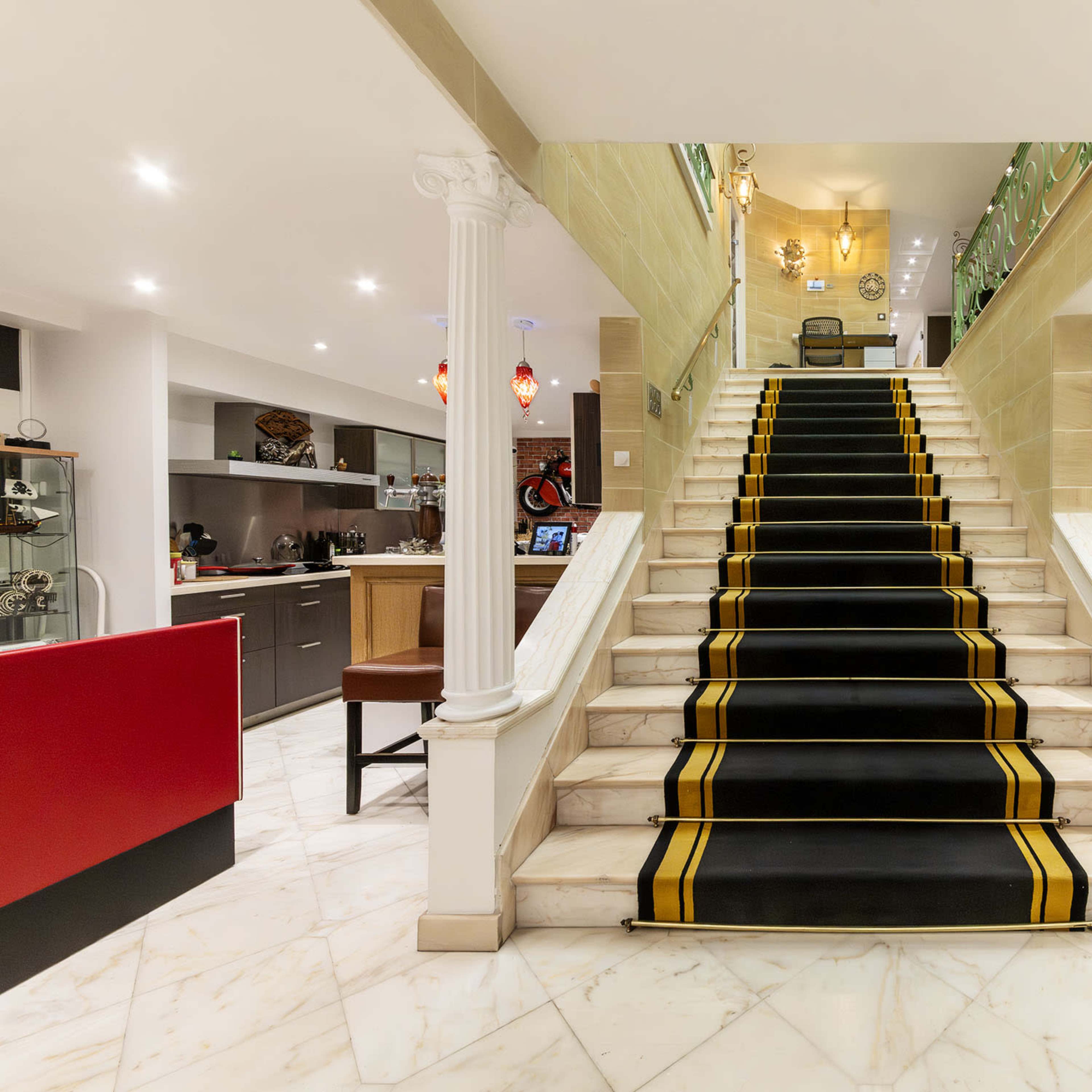 A staircase with a black carpet featuring yellow stripes, leading up to a well-lit upper floor, flanked by two white columns.