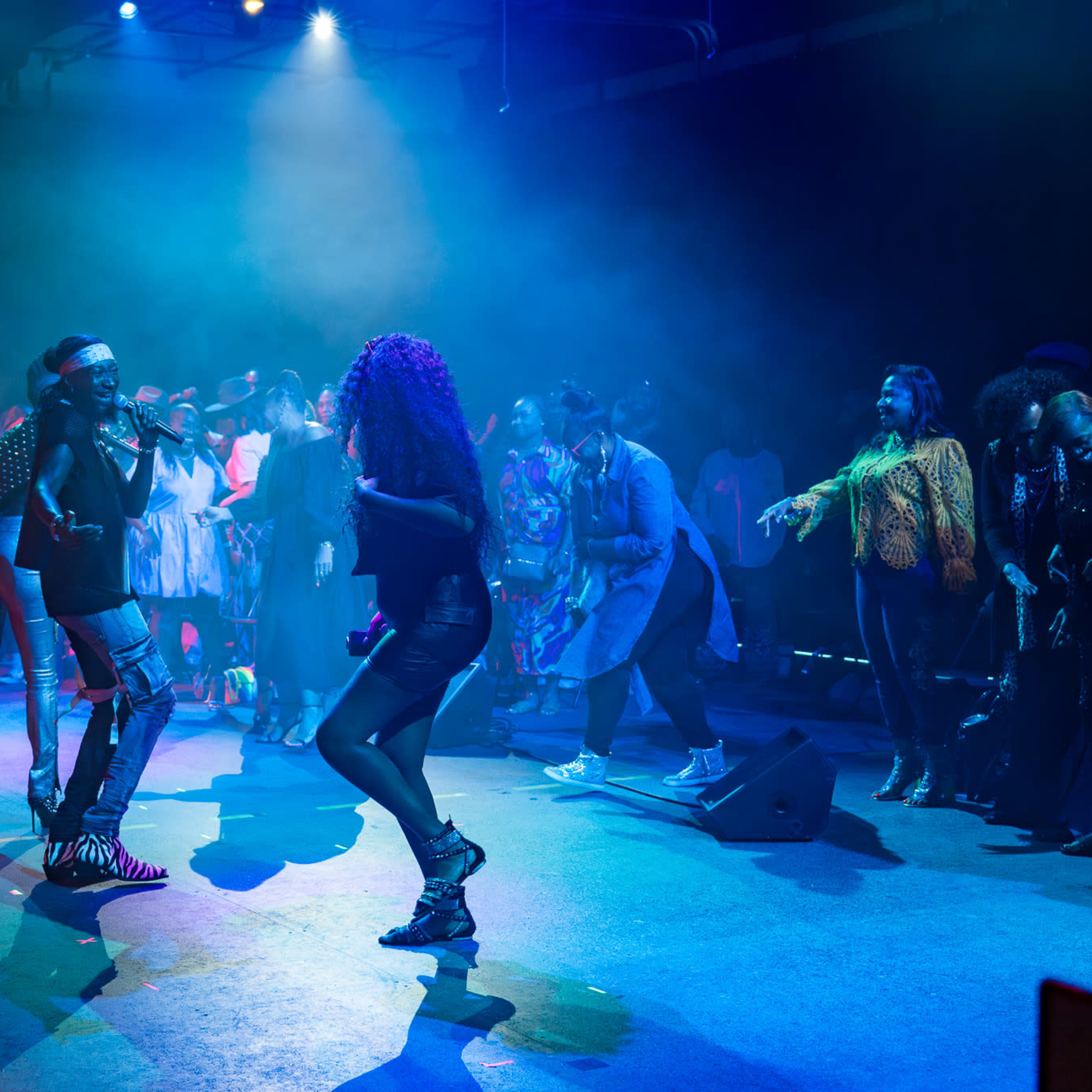 A performer sings on stage while audience members dance and engage with the music in a dimly lit venue.