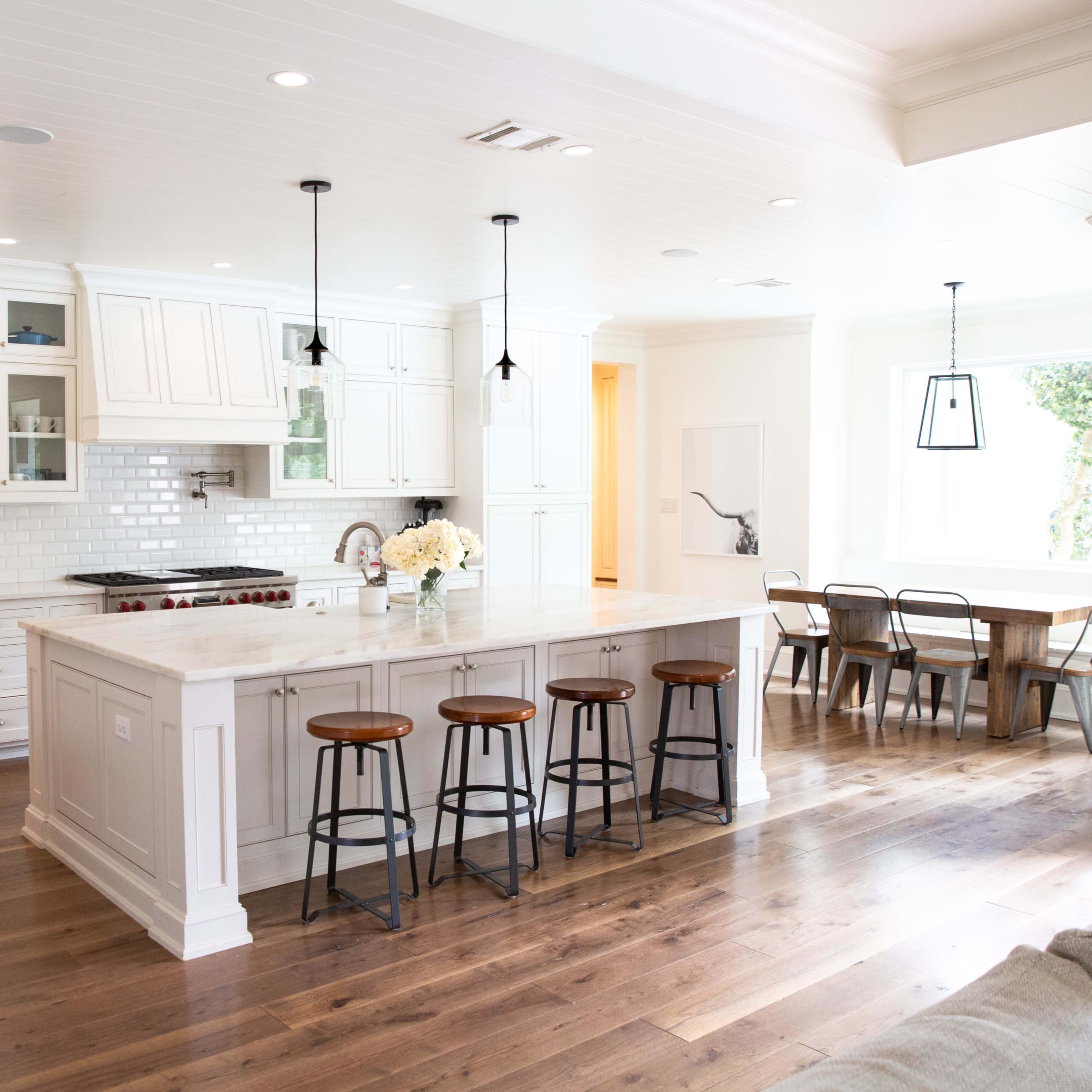 A modern kitchen with white cabinetry, a large marble island with bar stools, and an adjacent dining area with a wooden table and chairs.