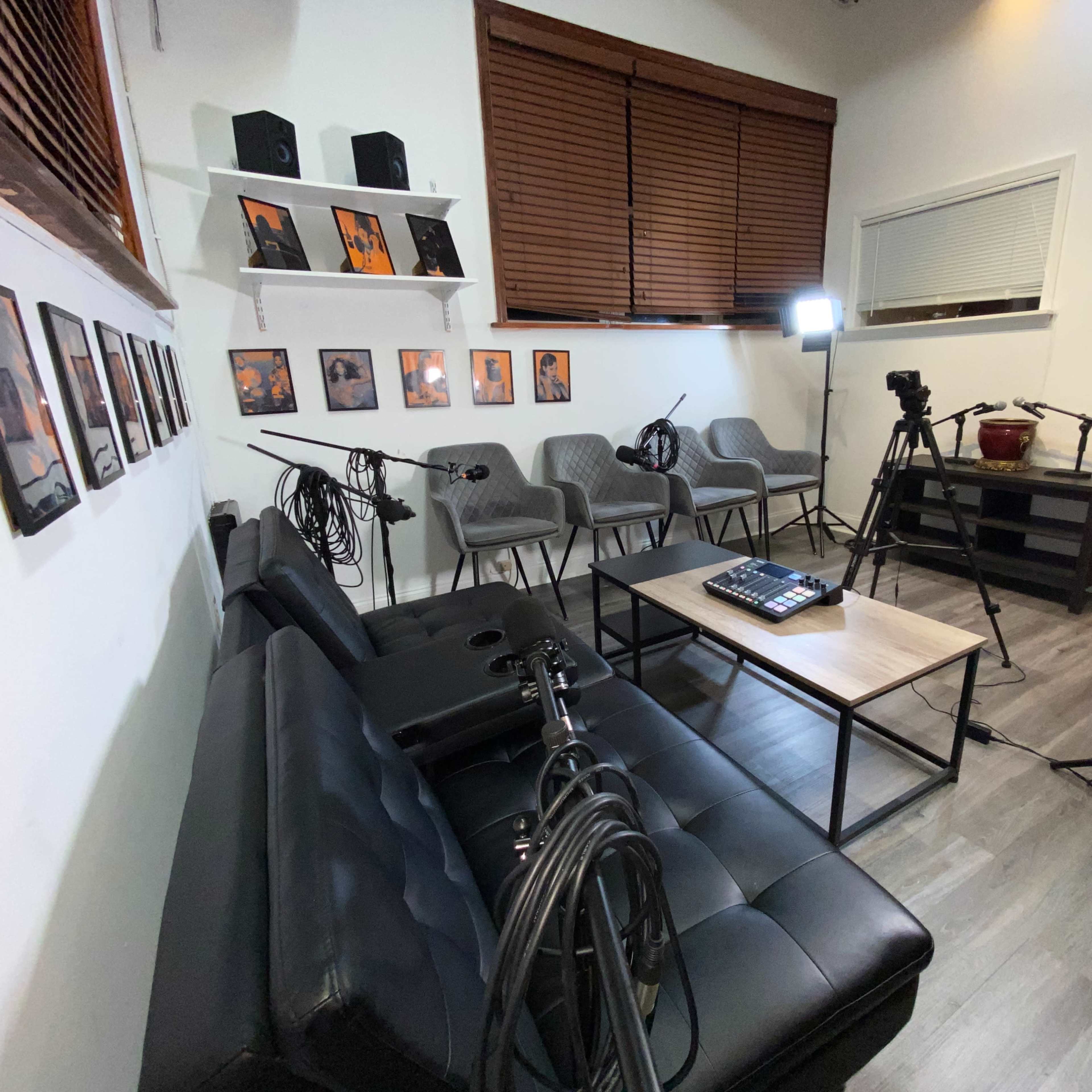 A modern room with a black couch, a coffee table, multiple microphones on stands, and several photography lights set up around empty gray chairs.