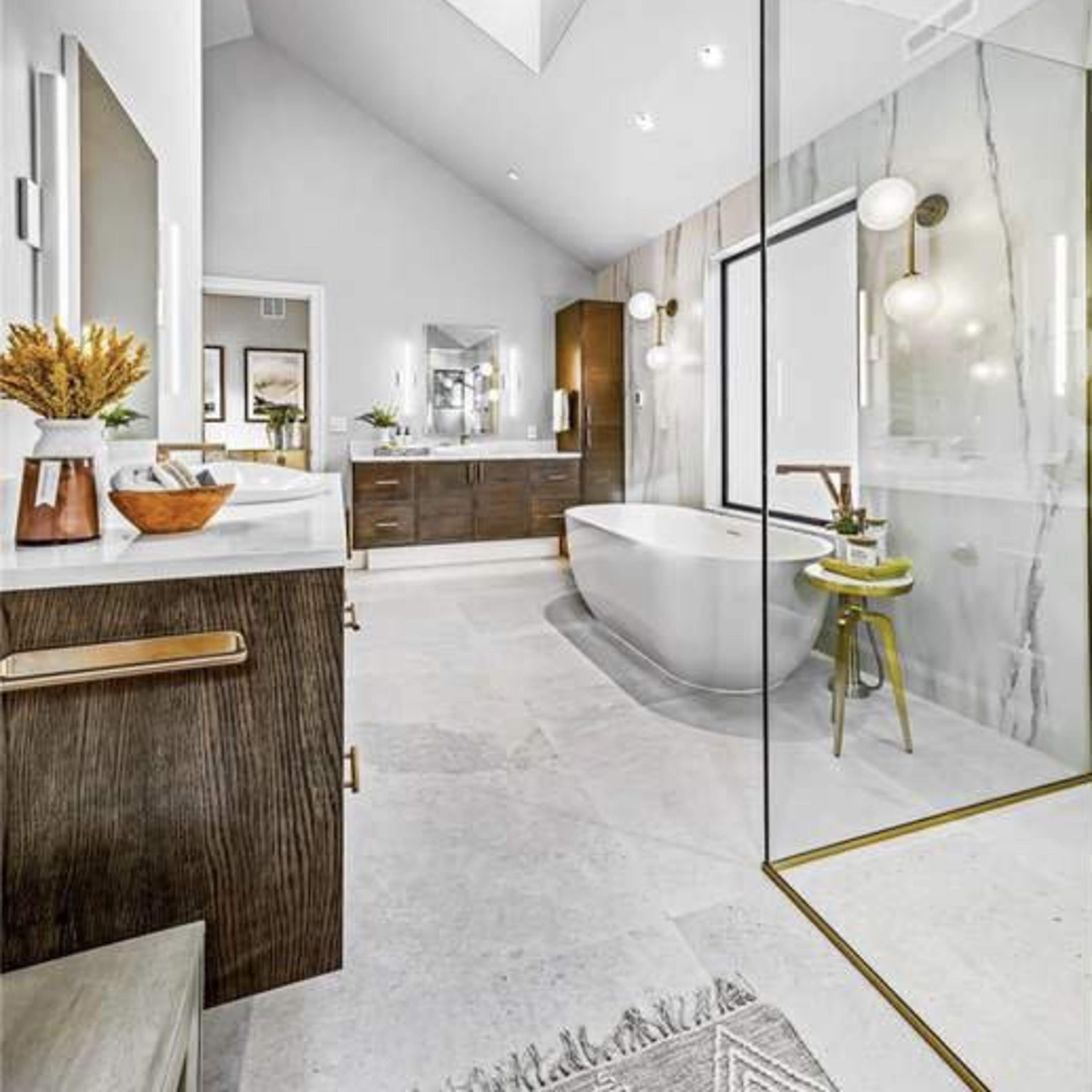A modern bathroom with a freestanding bathtub, dual vanities, a glass shower, and a skylight above.