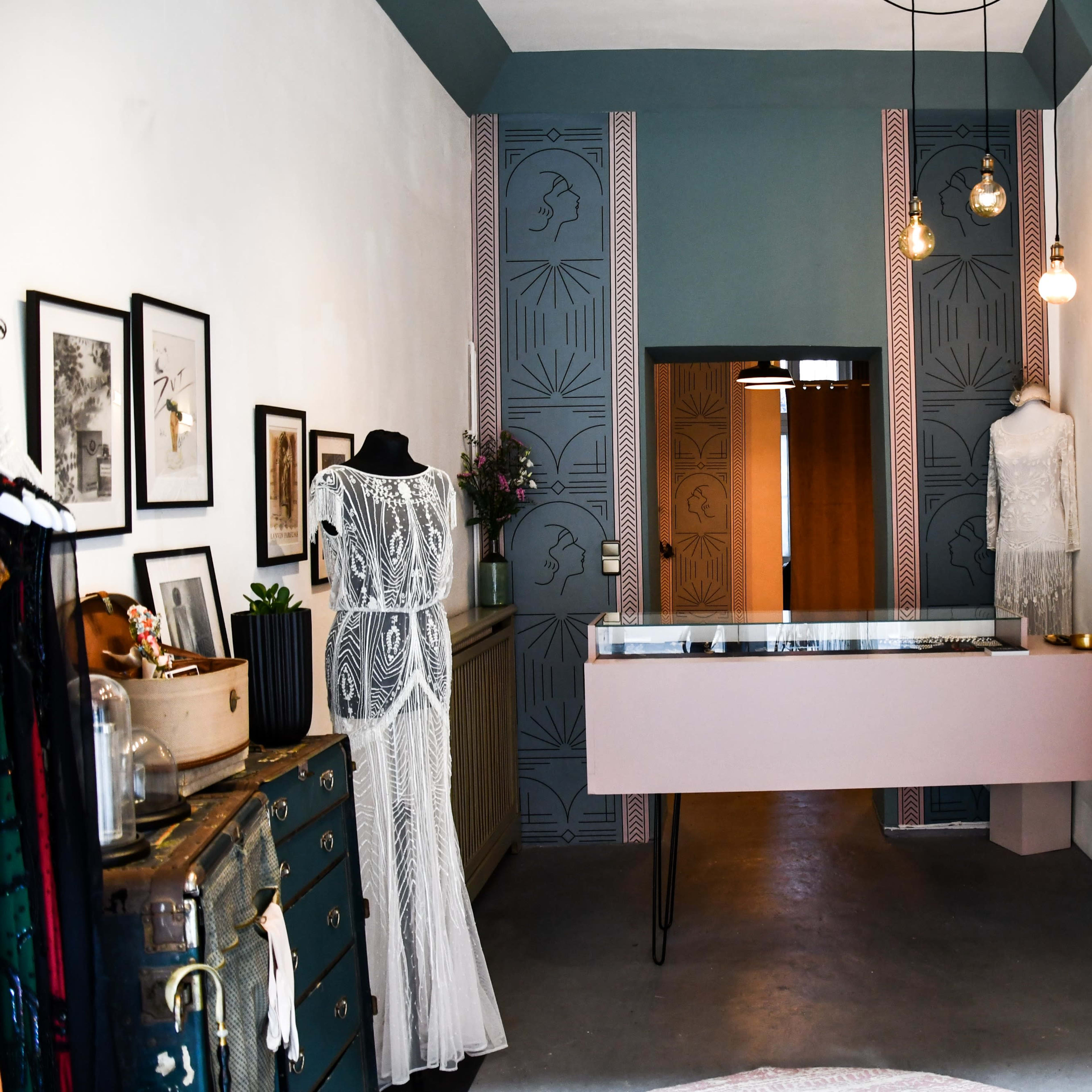 A modern boutique displaying elegant dresses, with a pale pink display counter, adorned walls, and various decor elements.