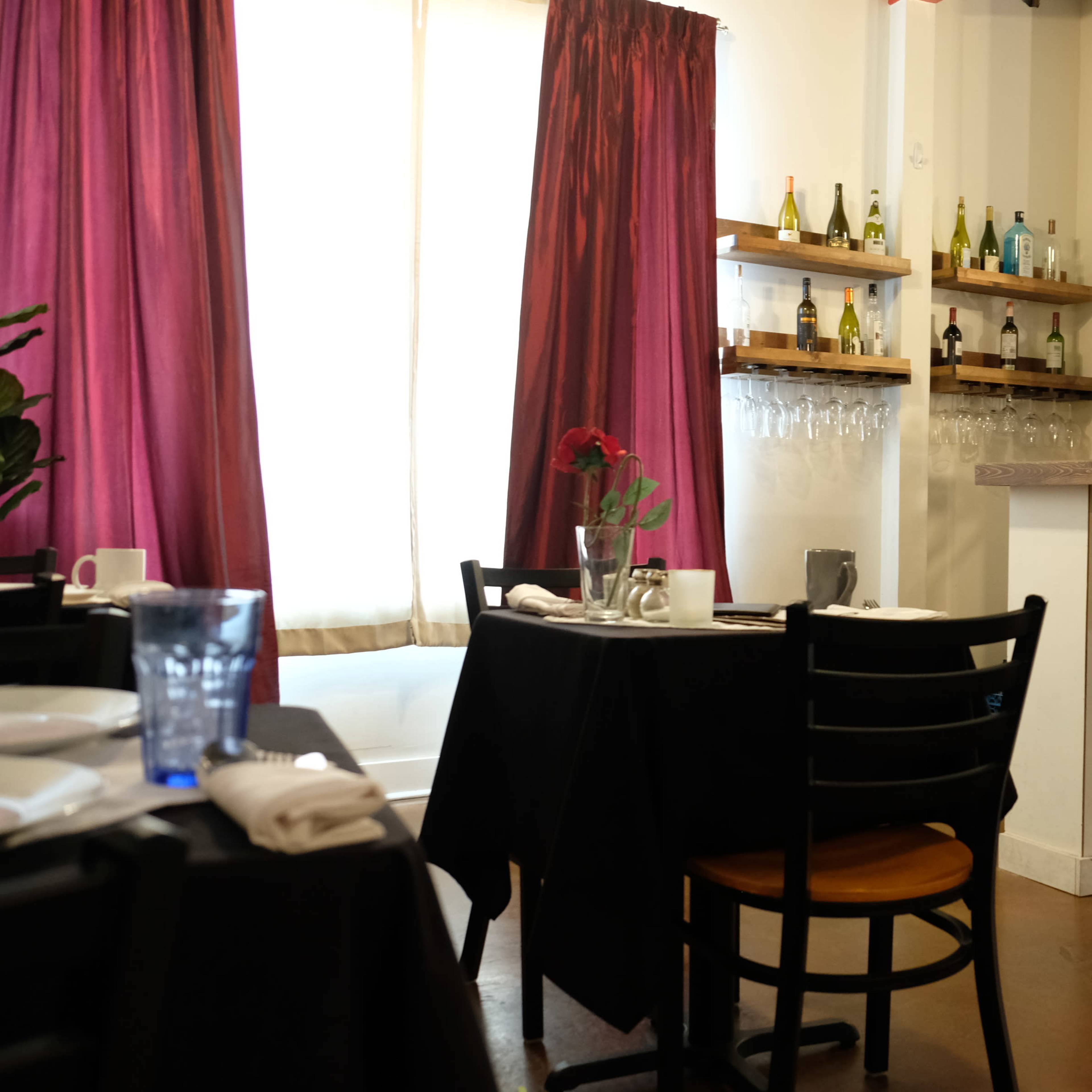 A restaurant interior featuring black tables, bar stools at a counter, and curtains in shades of red.