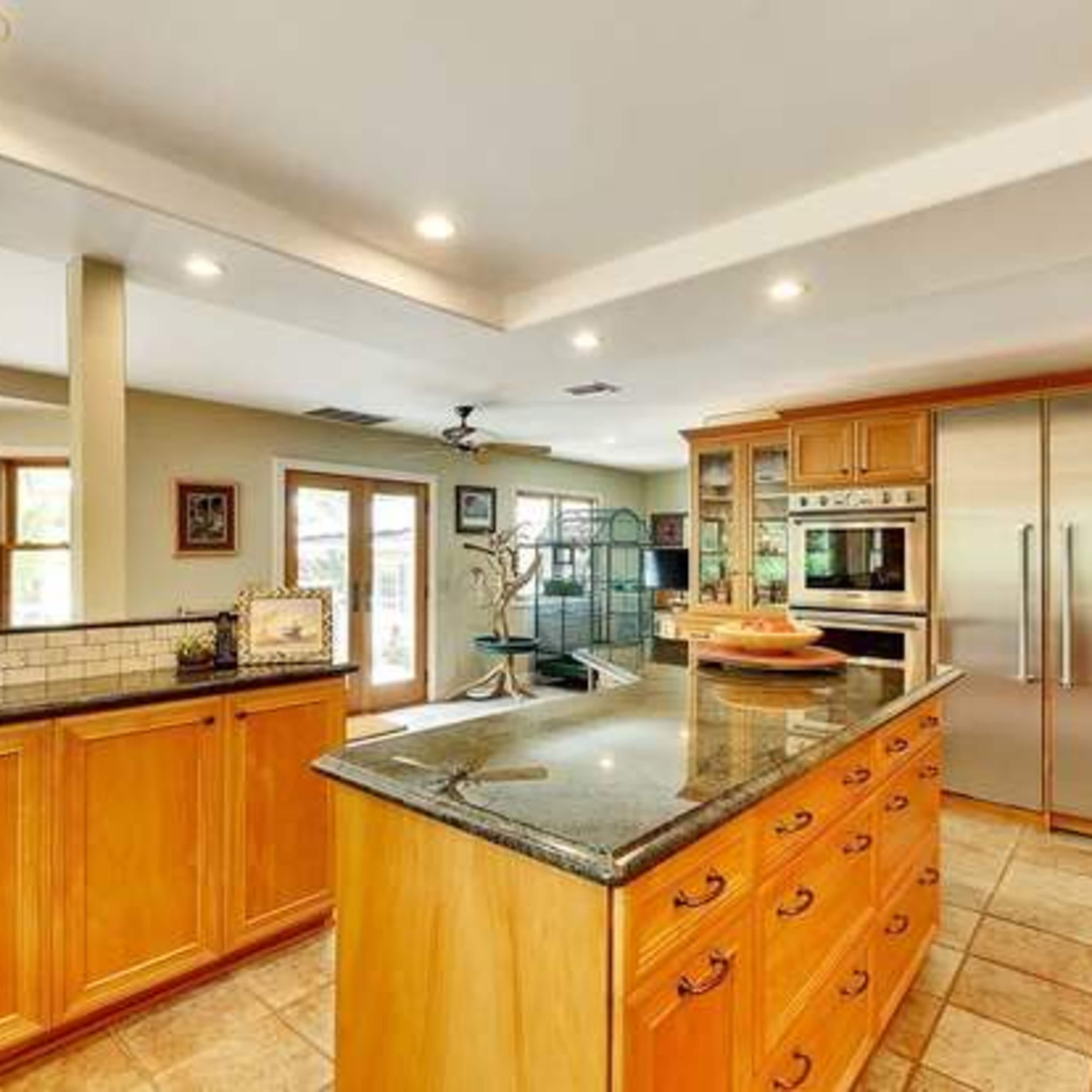 A spacious kitchen with wooden cabinetry, a large island with a granite countertop, and stainless steel appliances.
