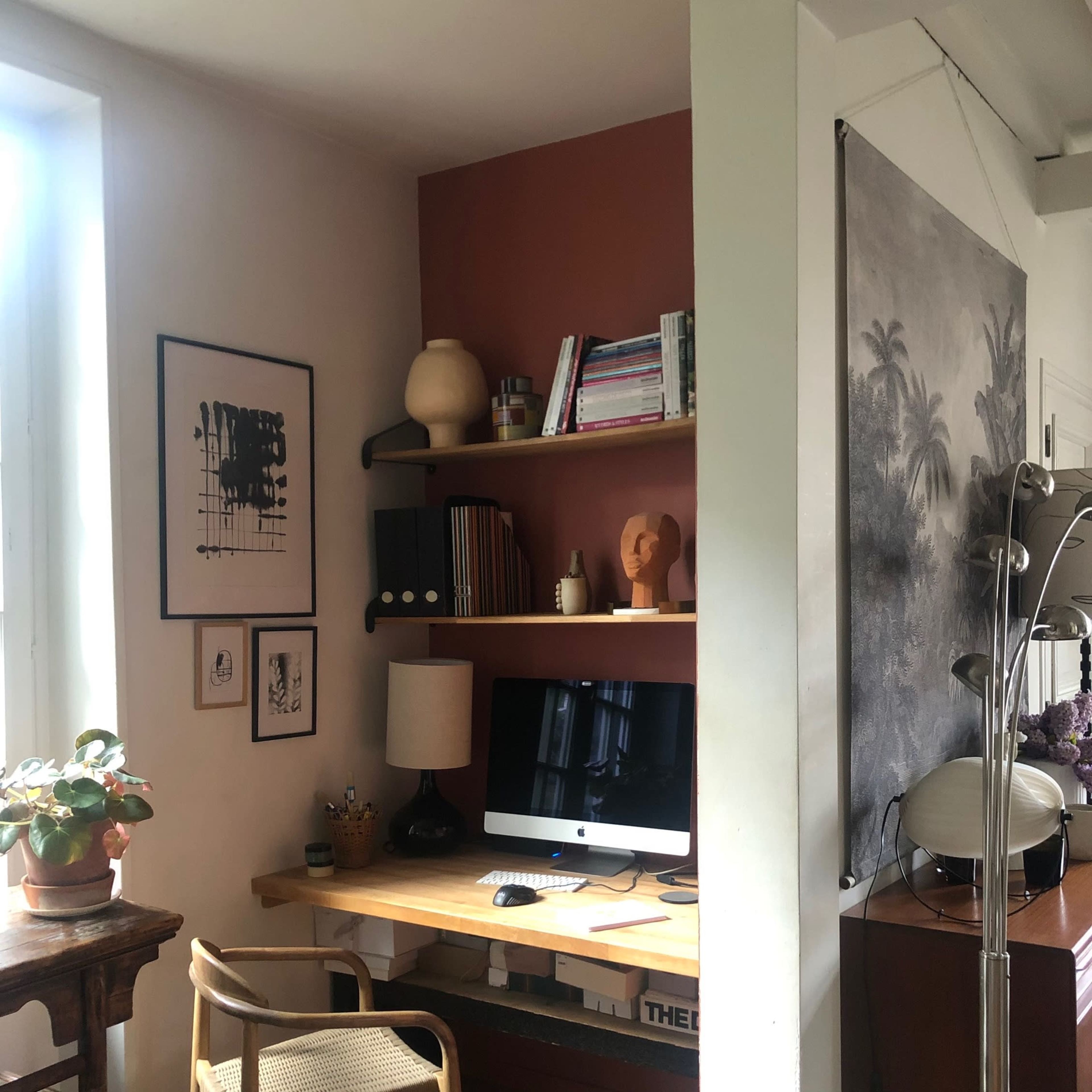 A well-organized home office with a desk, an iMac, shelves filled with books and decor, and a plant in the corner.