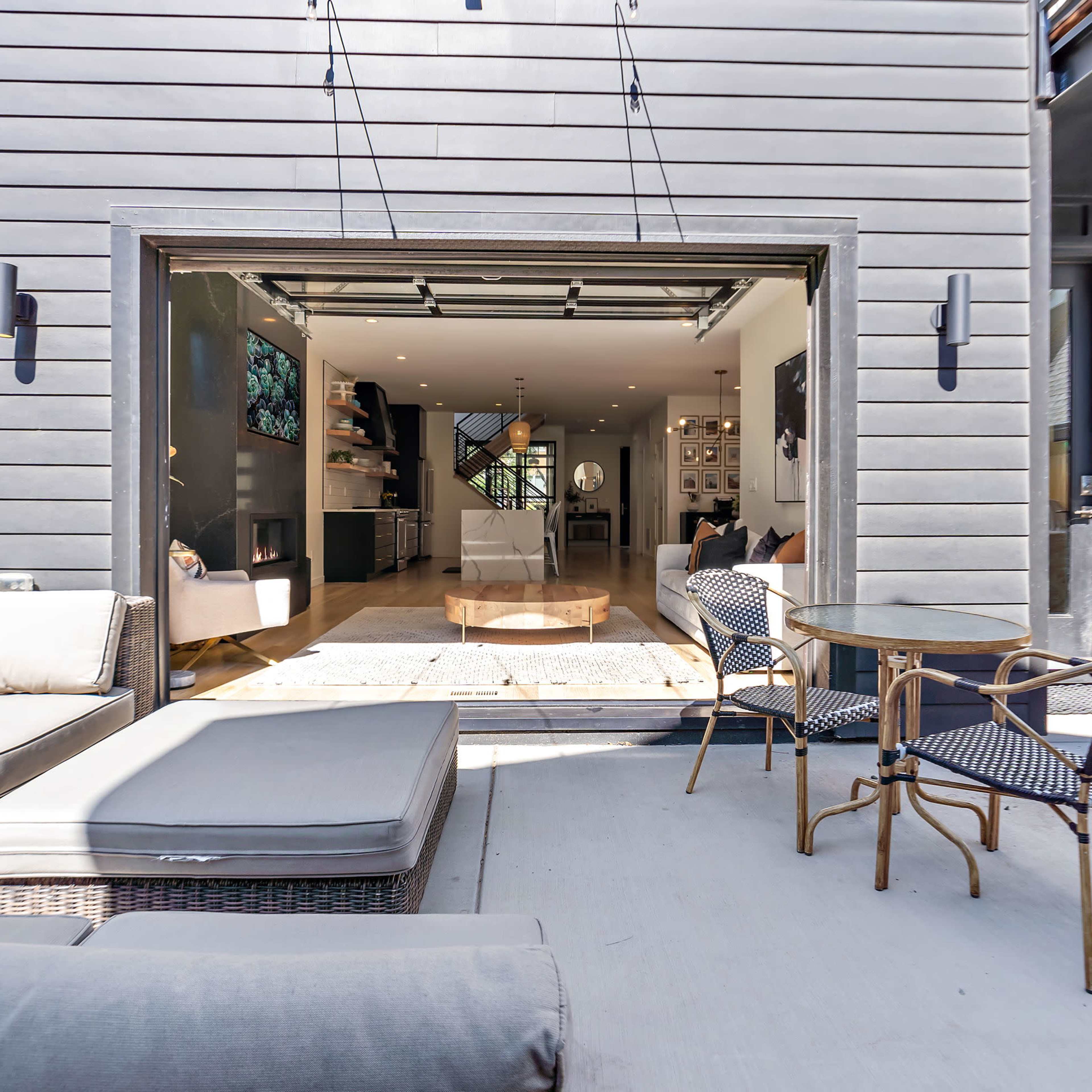 A spacious outdoor patio area with a sectional sofa and a small dining table, leading to an open interior space with a large folding door.