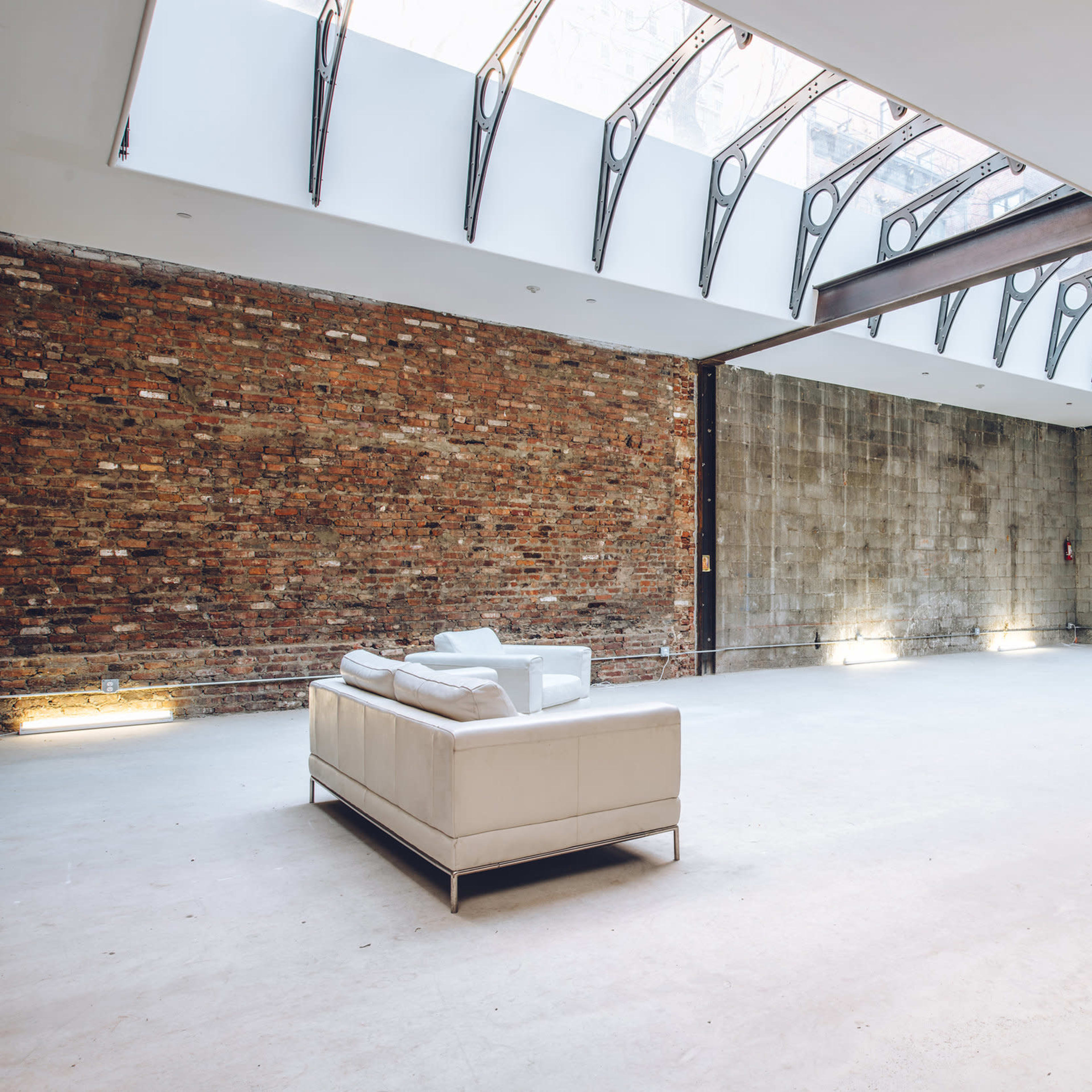 A spacious interior with exposed brick walls, a concrete floor, and a white leather sofa under a skylight.