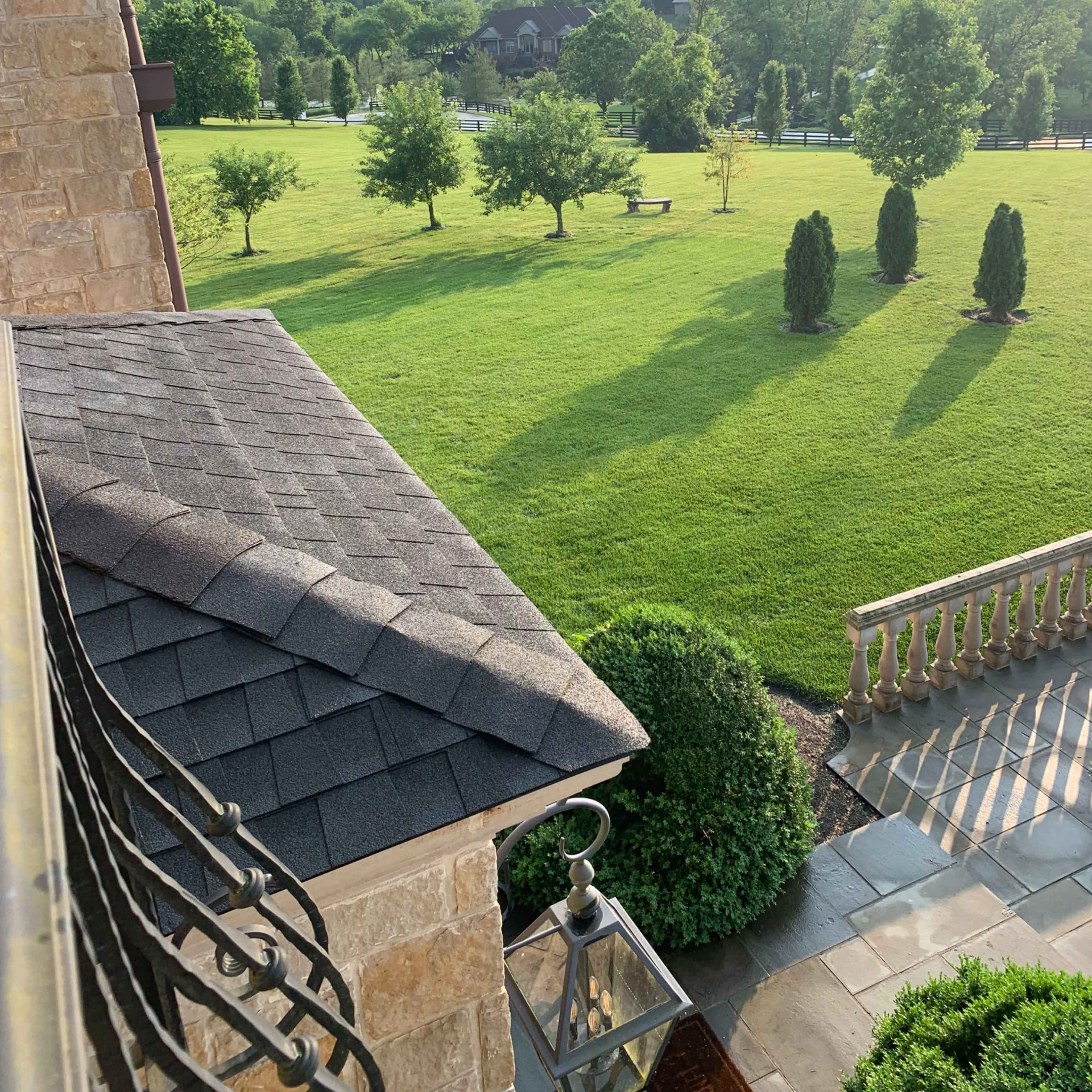 A view from a balcony overlooking a lush green lawn with several trees and a large field in the background.