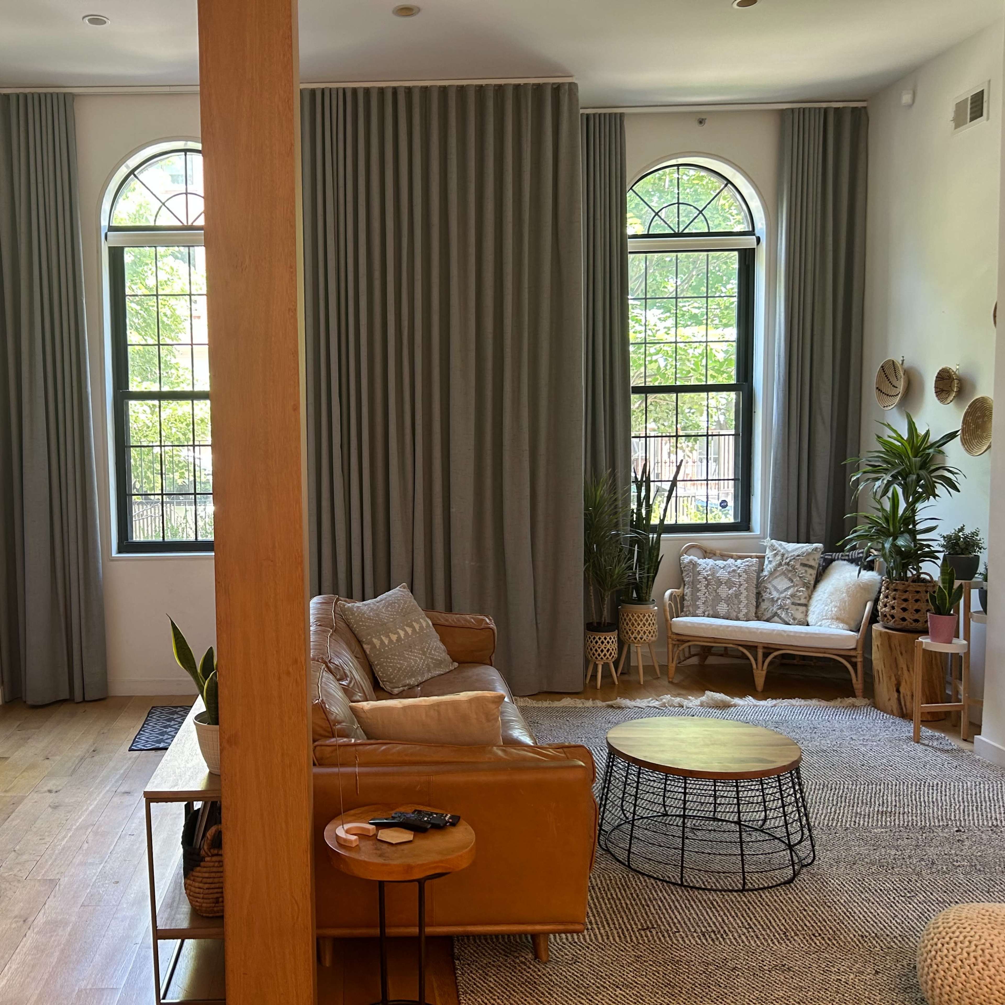 A welcoming living room with large windows, a beige sofa, a round coffee table, and decorative plants, divided by a wooden support beam.