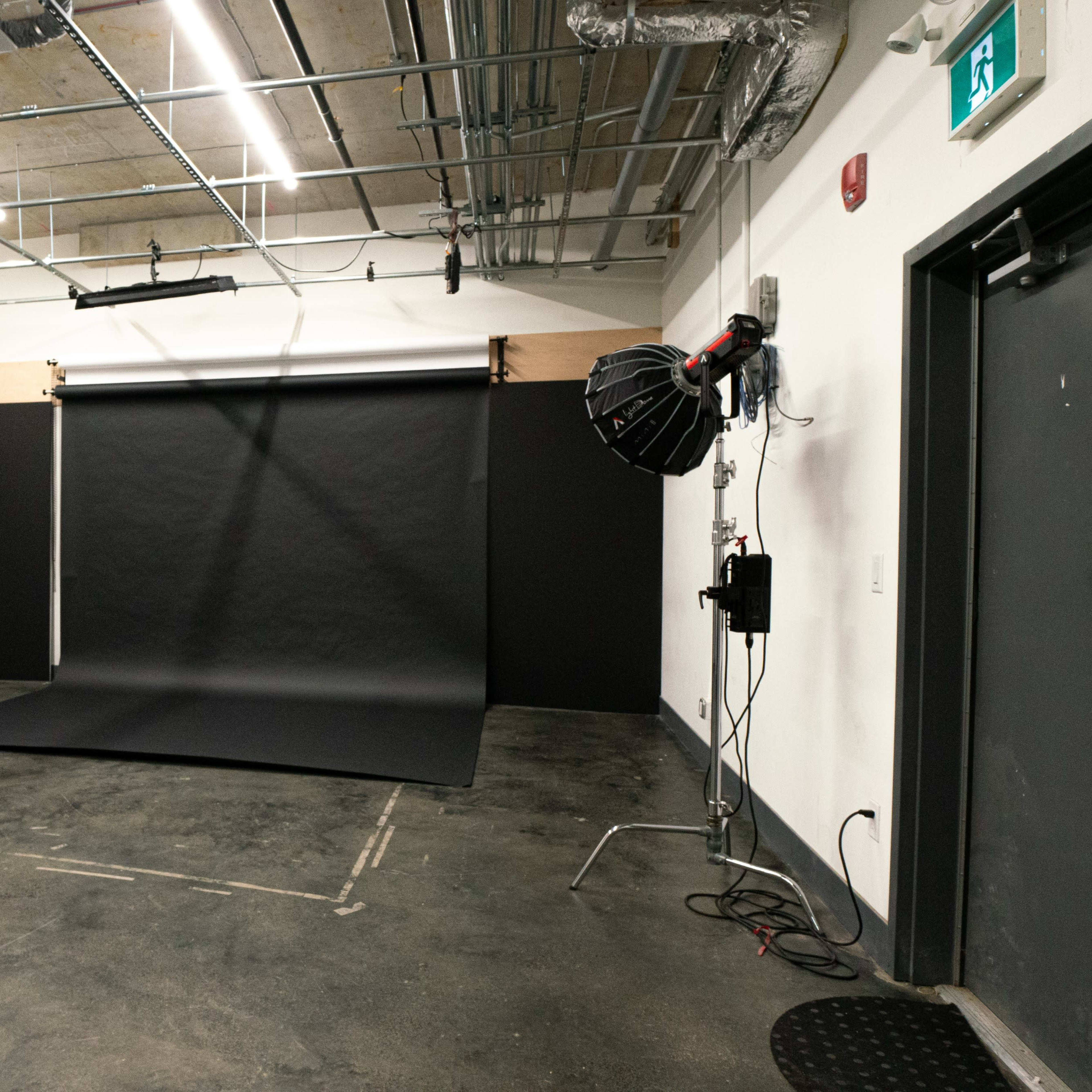A photography studio with a black backdrop, a lighting setup, and a smooth concrete floor.