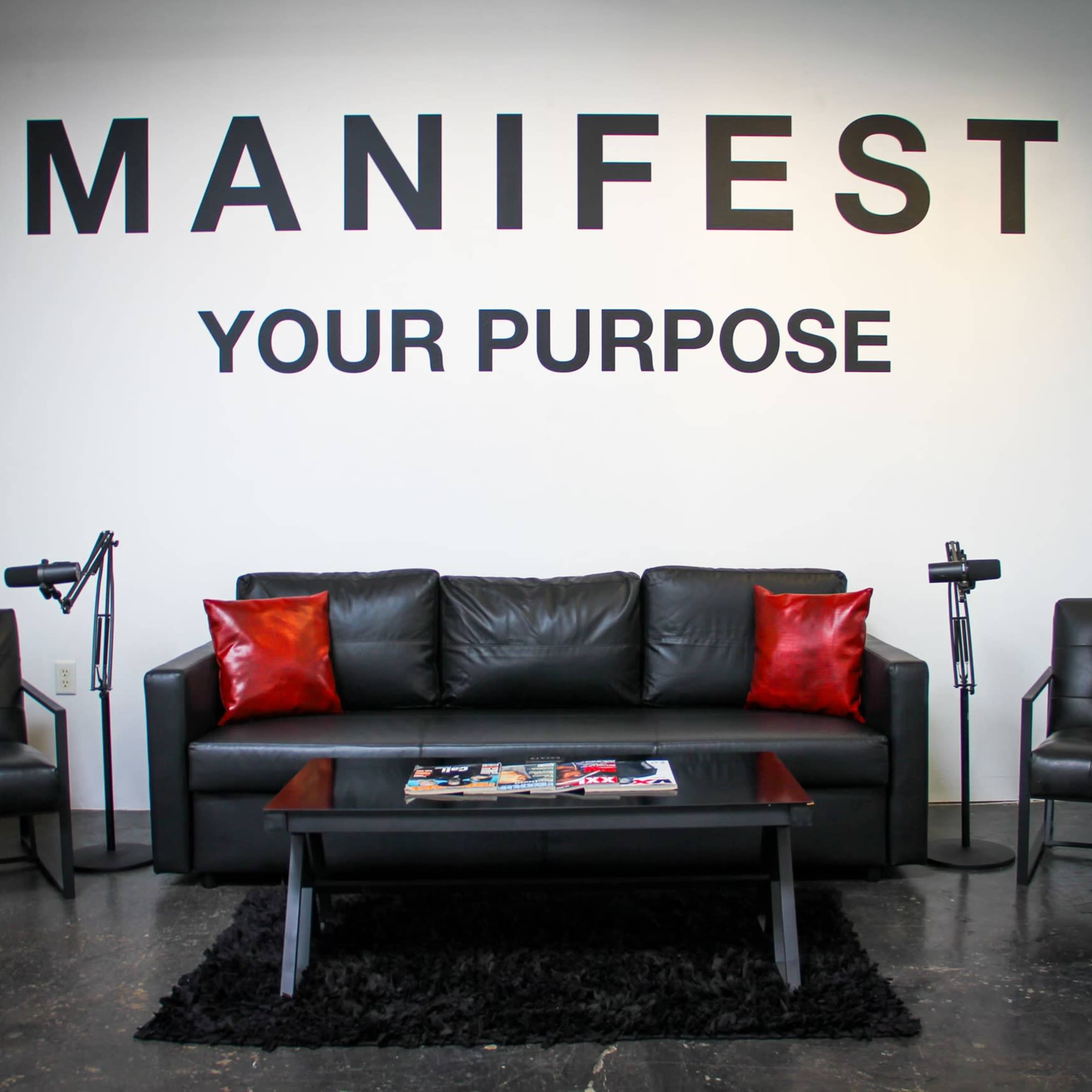 A modern seating area with a black sofa, two black armchairs, a coffee table, and a wall display featuring the text "MANIFEST YOUR PURPOSE."
