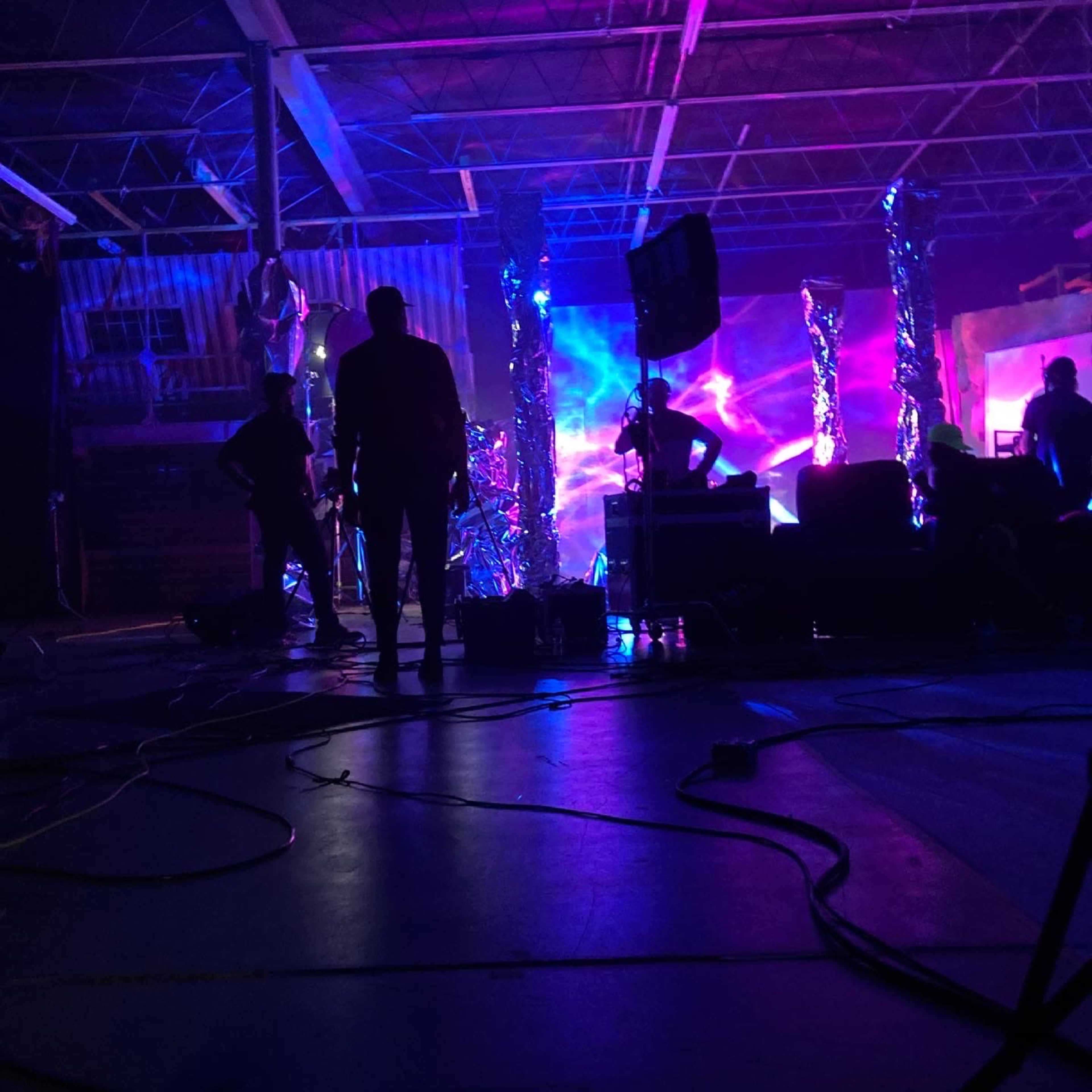 A group of silhouetted figures work in a dimly lit space filled with colorful, dynamic lighting effects and equipment.