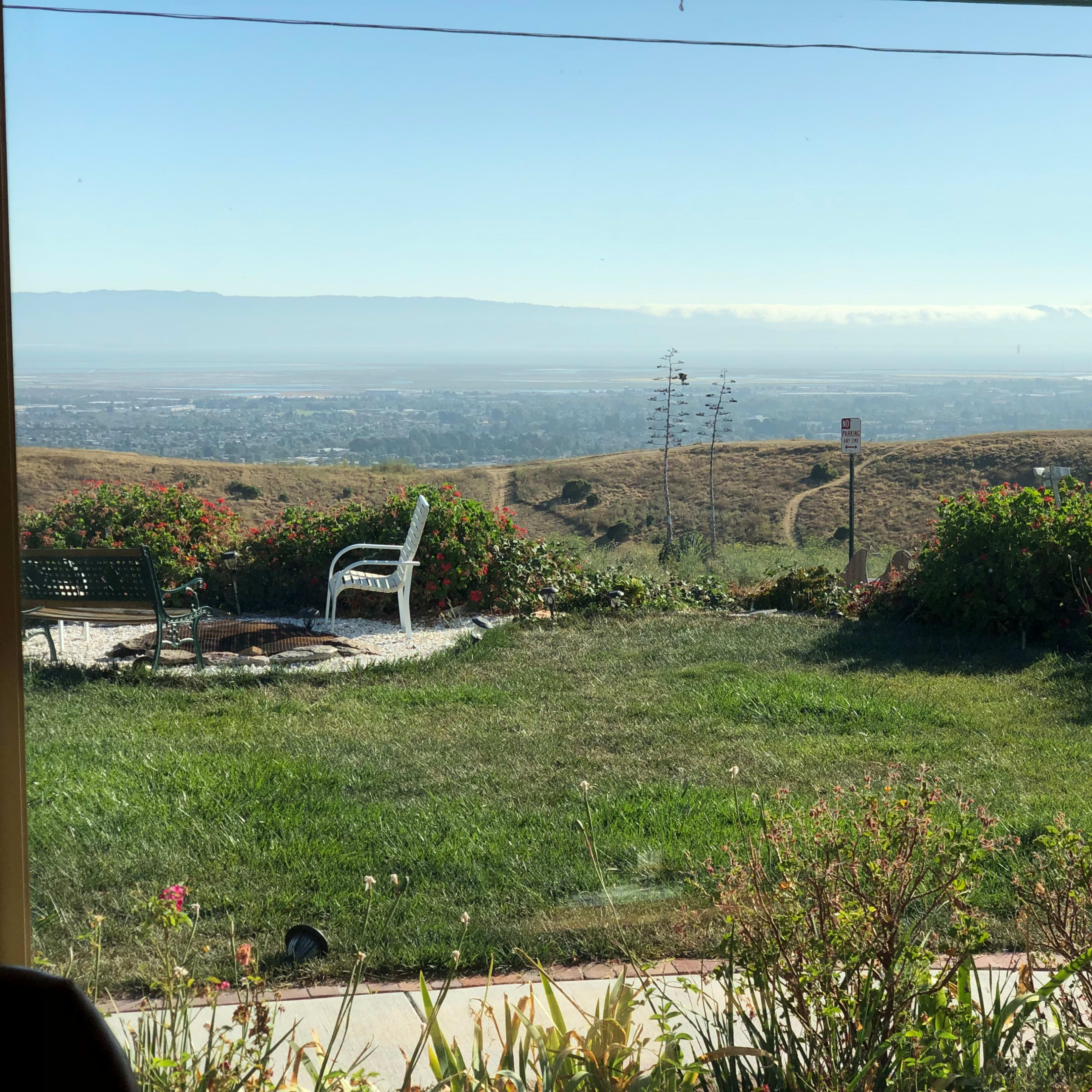 A view from a porch overlooking a grassy landscape that slopes down to a valley with distant hills in the background.