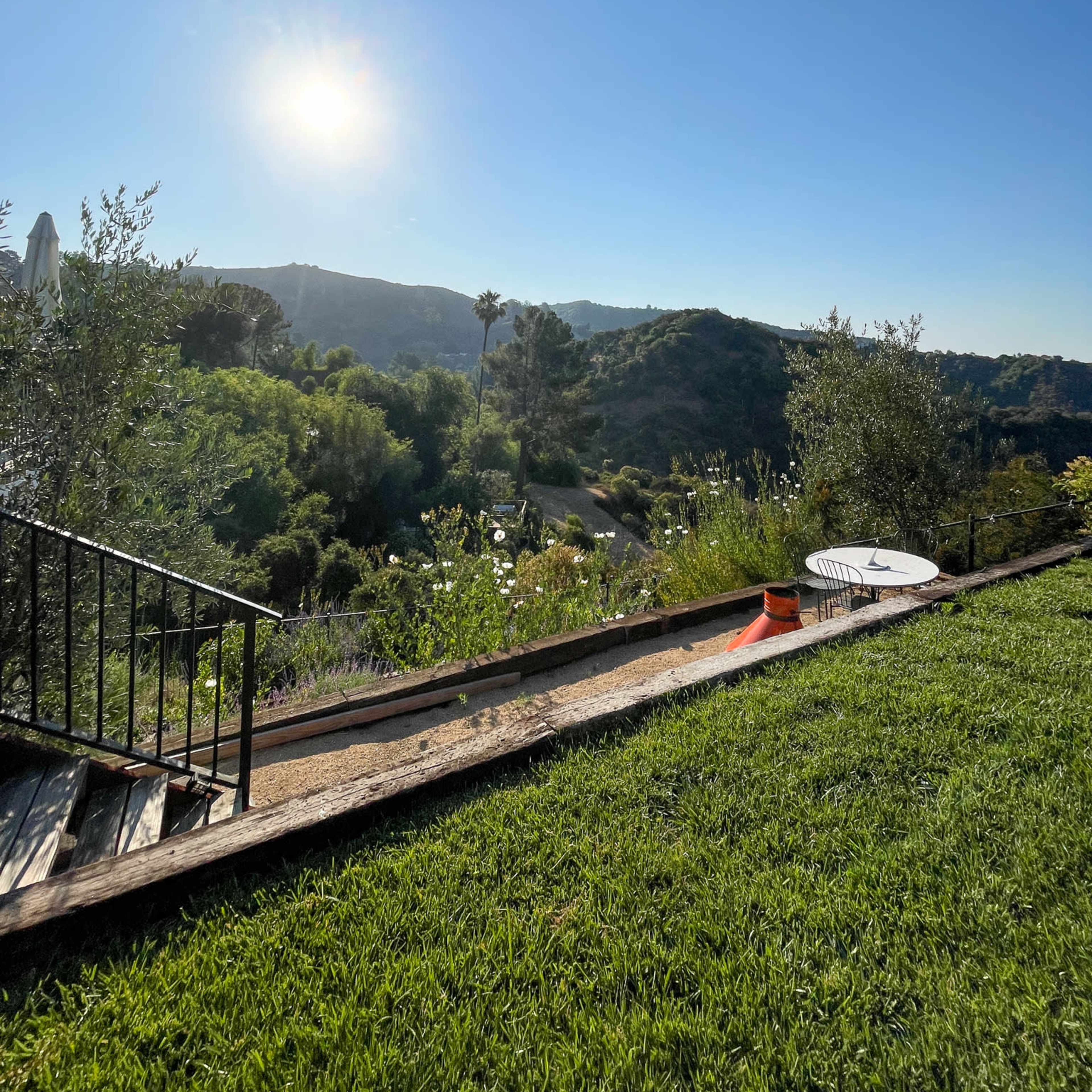 A landscaped yard with a pathway leading to a view of hills and a clear blue sky.