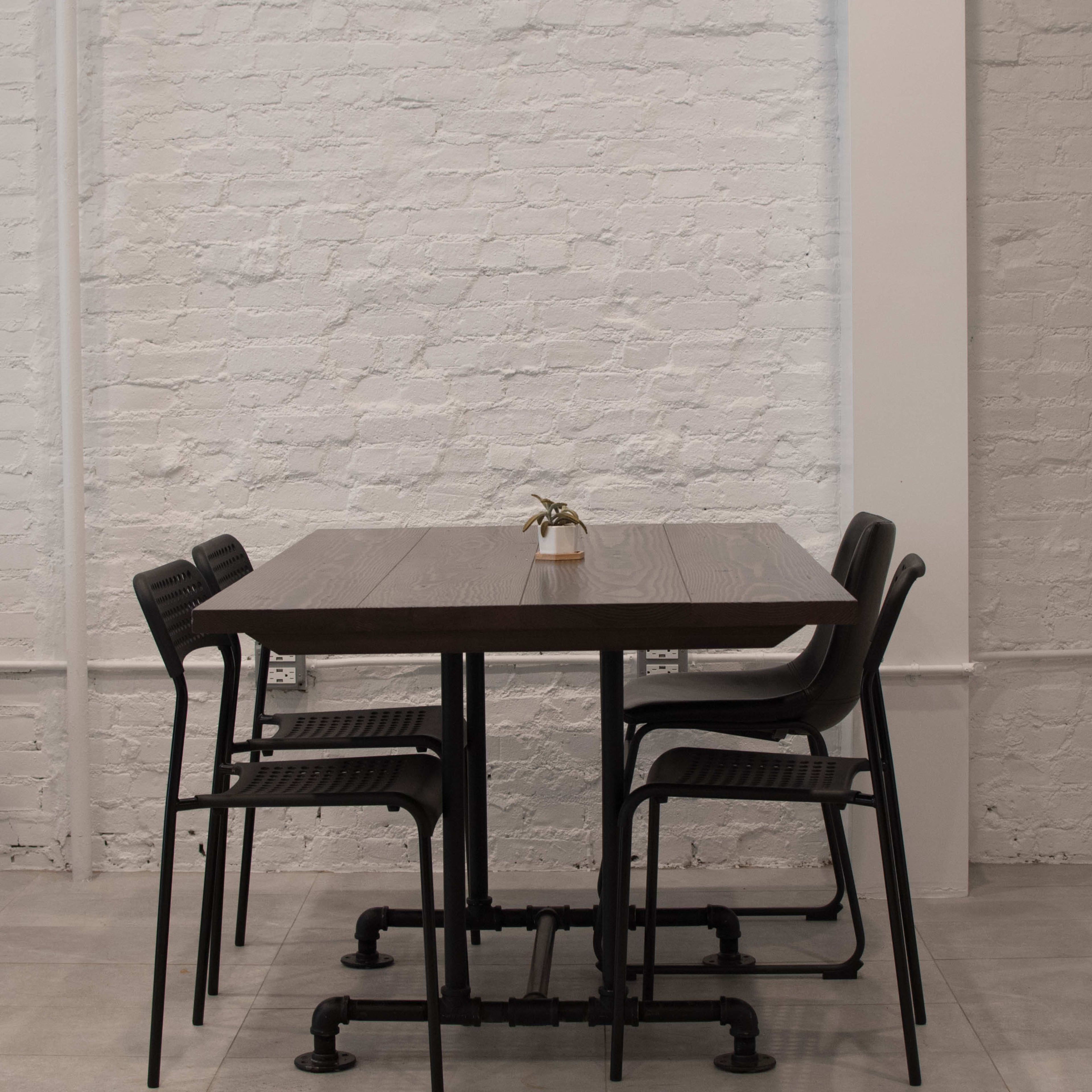 A simple table with chairs is positioned against a white brick wall, with a small plant on the table.