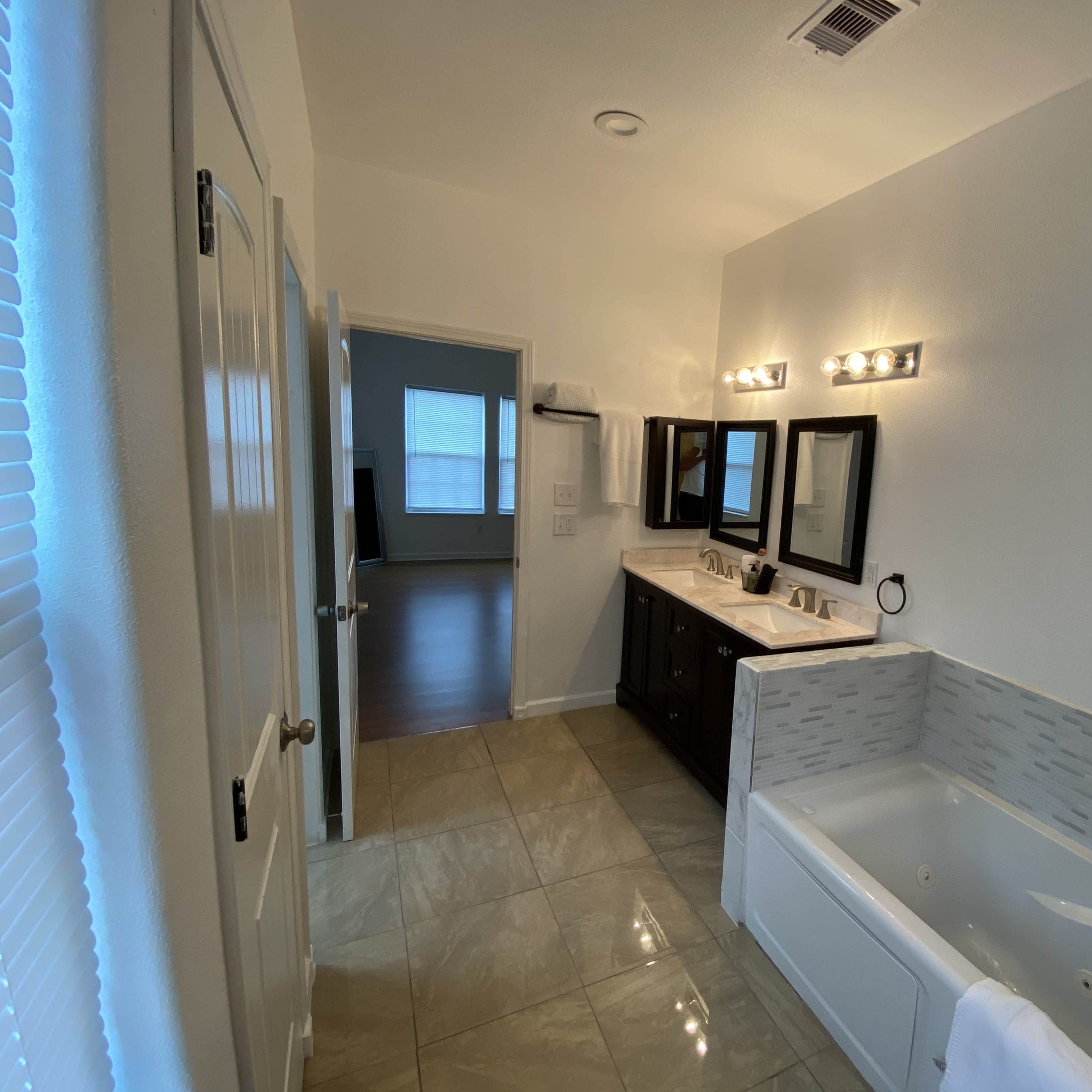 A modern bathroom with a dual-sink vanity, three mirrors, a tub, and tile flooring.
