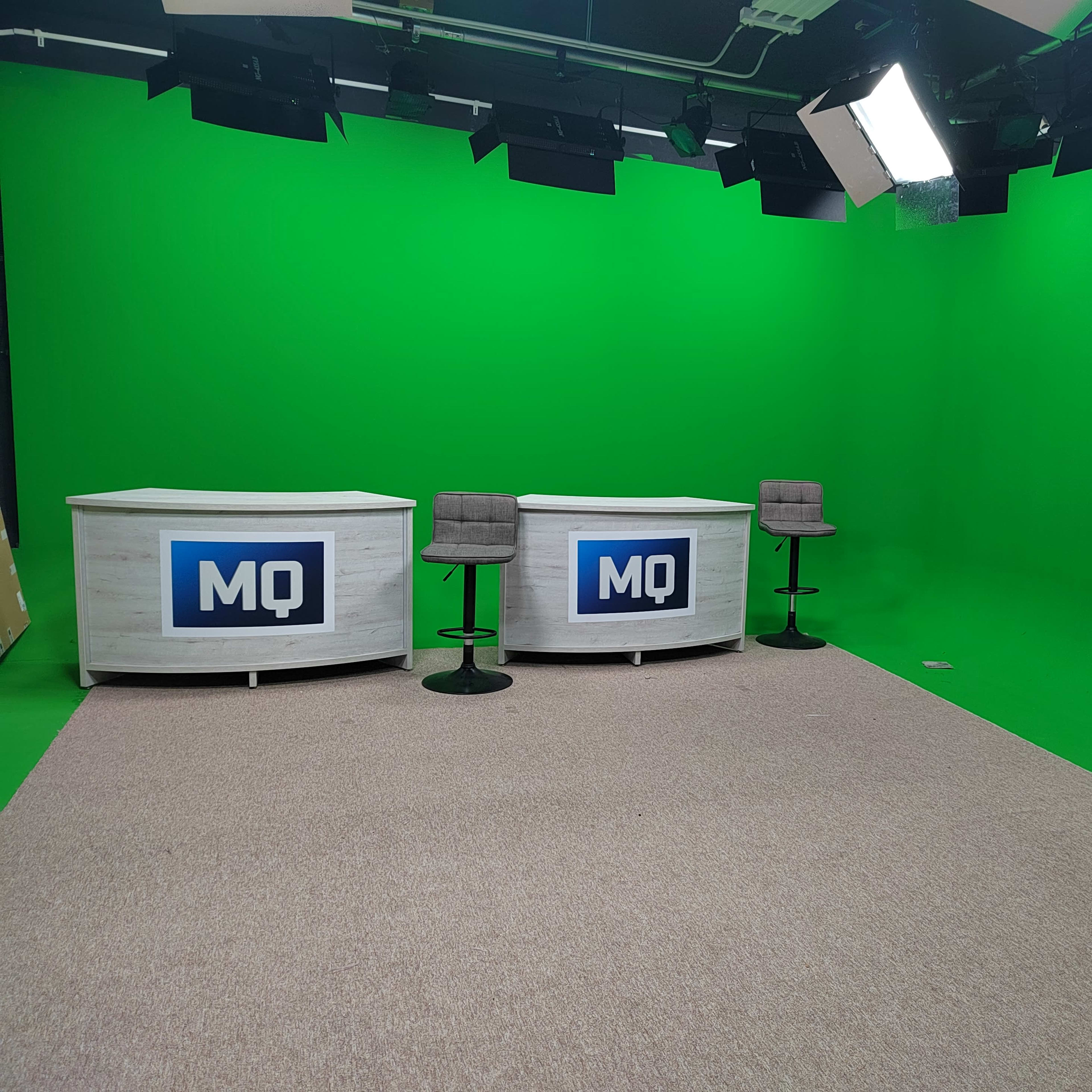A green screen studio setup with two white desks and bar stools.