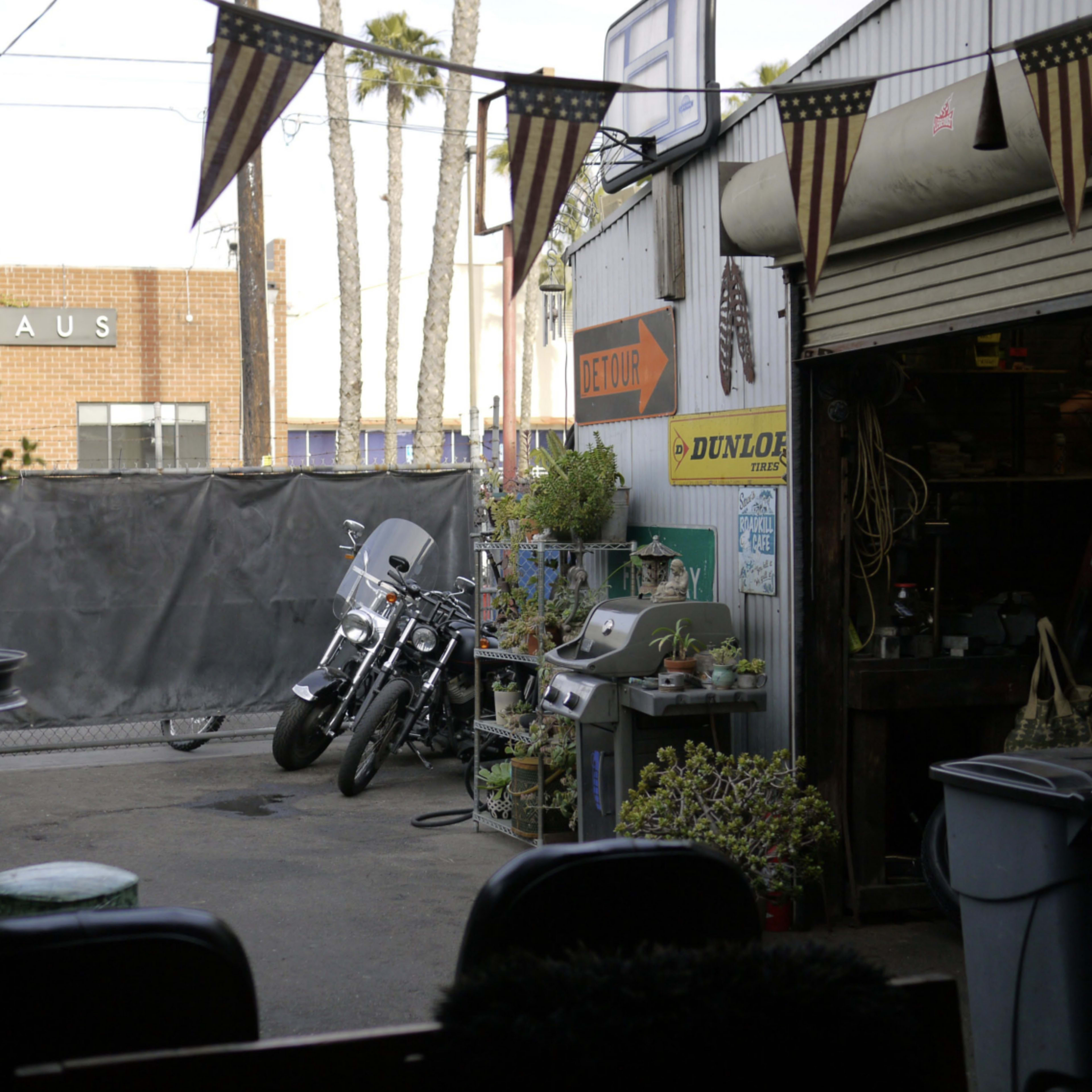 A patio area with a motorcycle parked beside various plants and outdoor furniture, adjacent to a wall displaying a large sign.