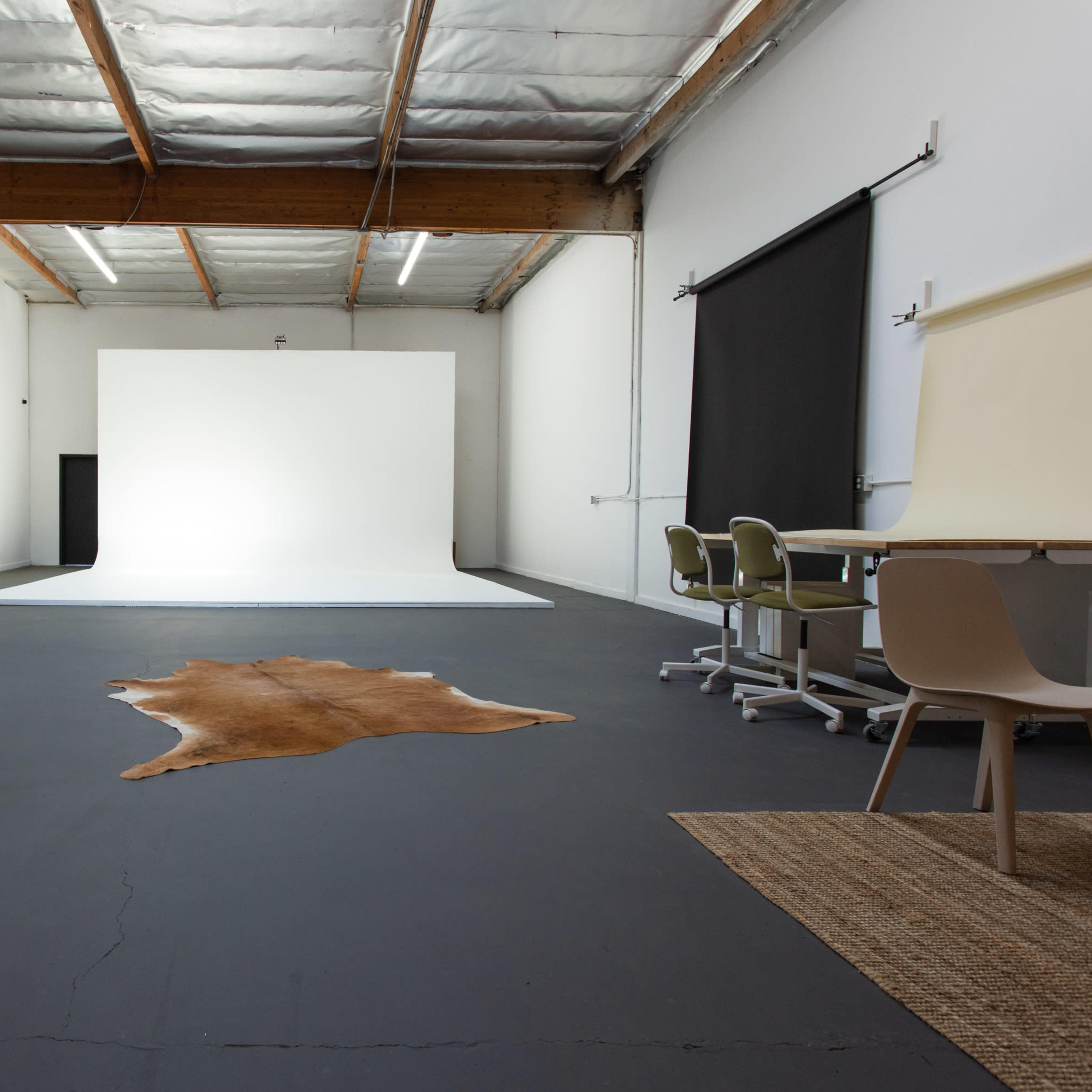 A spacious photography studio features a white backdrop, a cowhide rug on the floor, and several chairs arranged at a table.