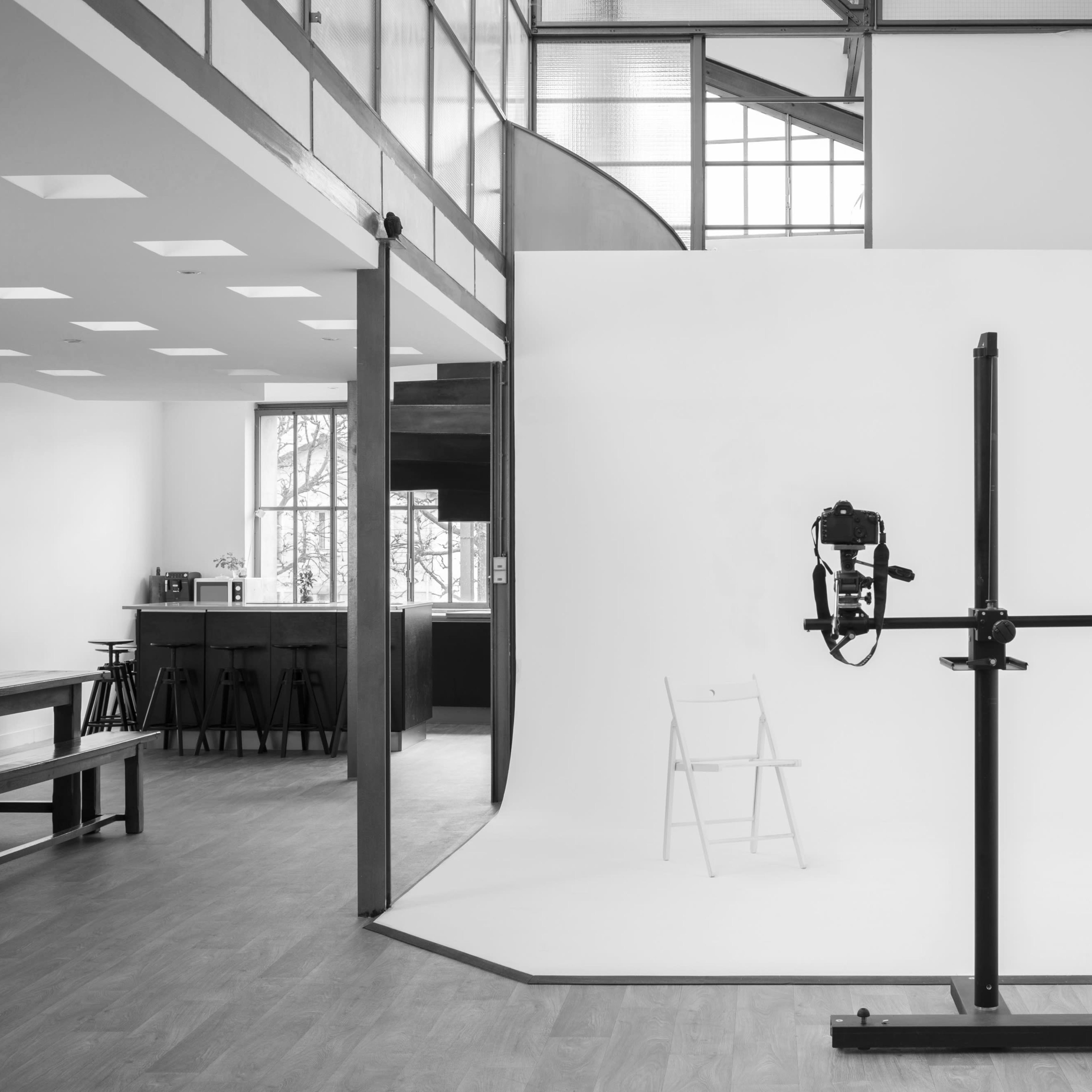 A photography studio with a white backdrop, a chair, and lighting equipment set up in a spacious room with modern architectural features.