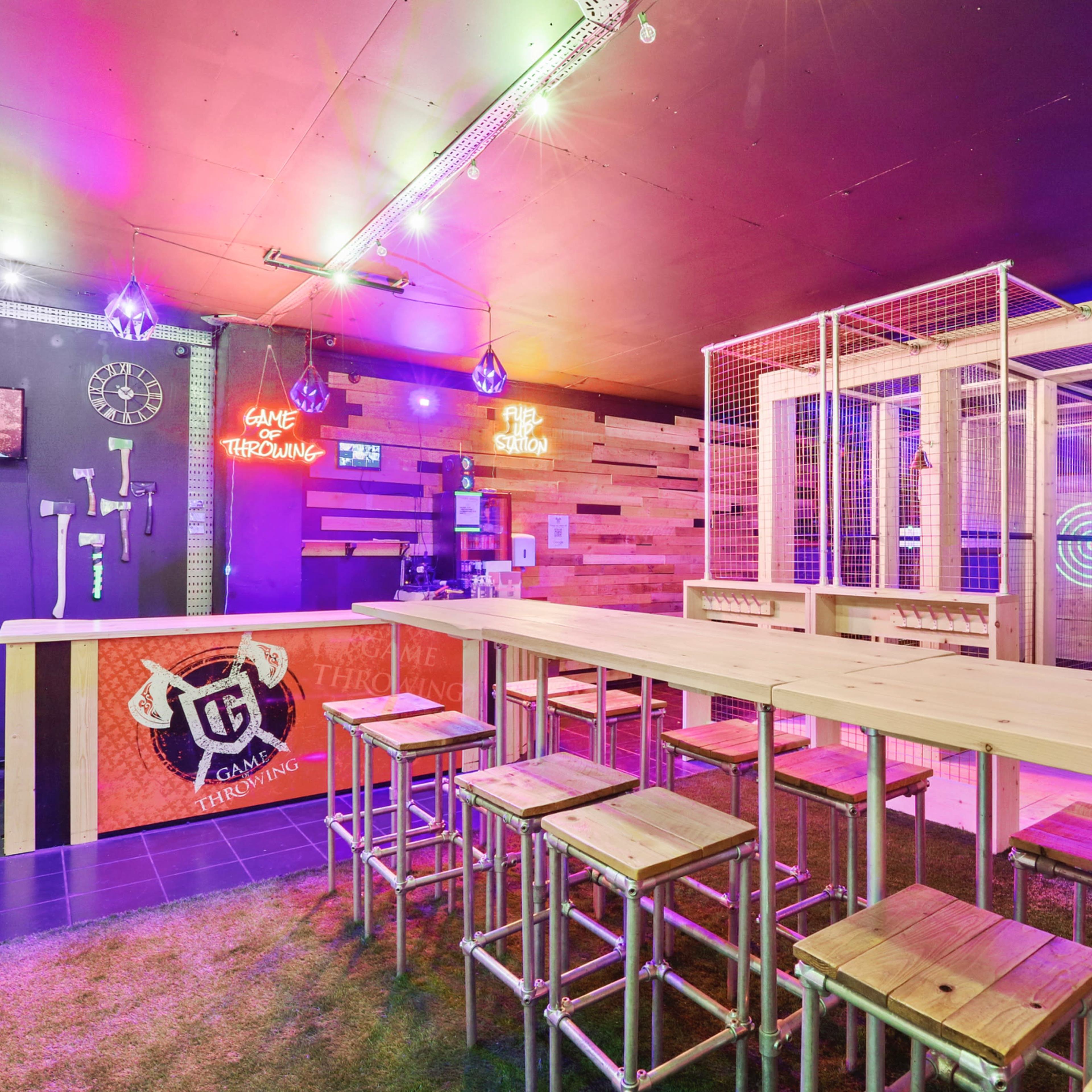A modern gaming lounge with a wooden bar, stools, and illuminated targets on the walls.