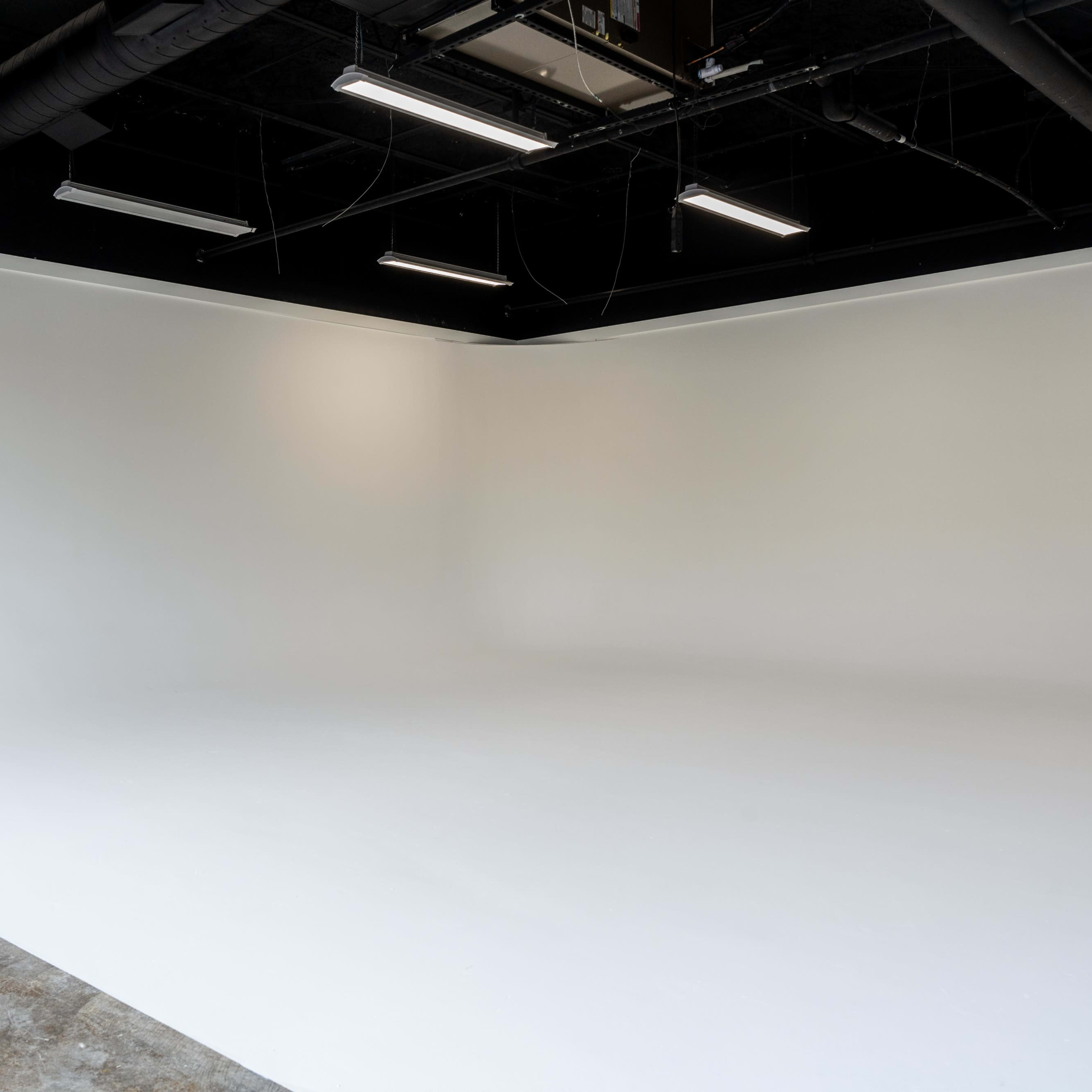 A spacious, empty studio with a white seamless background and a concrete floor.