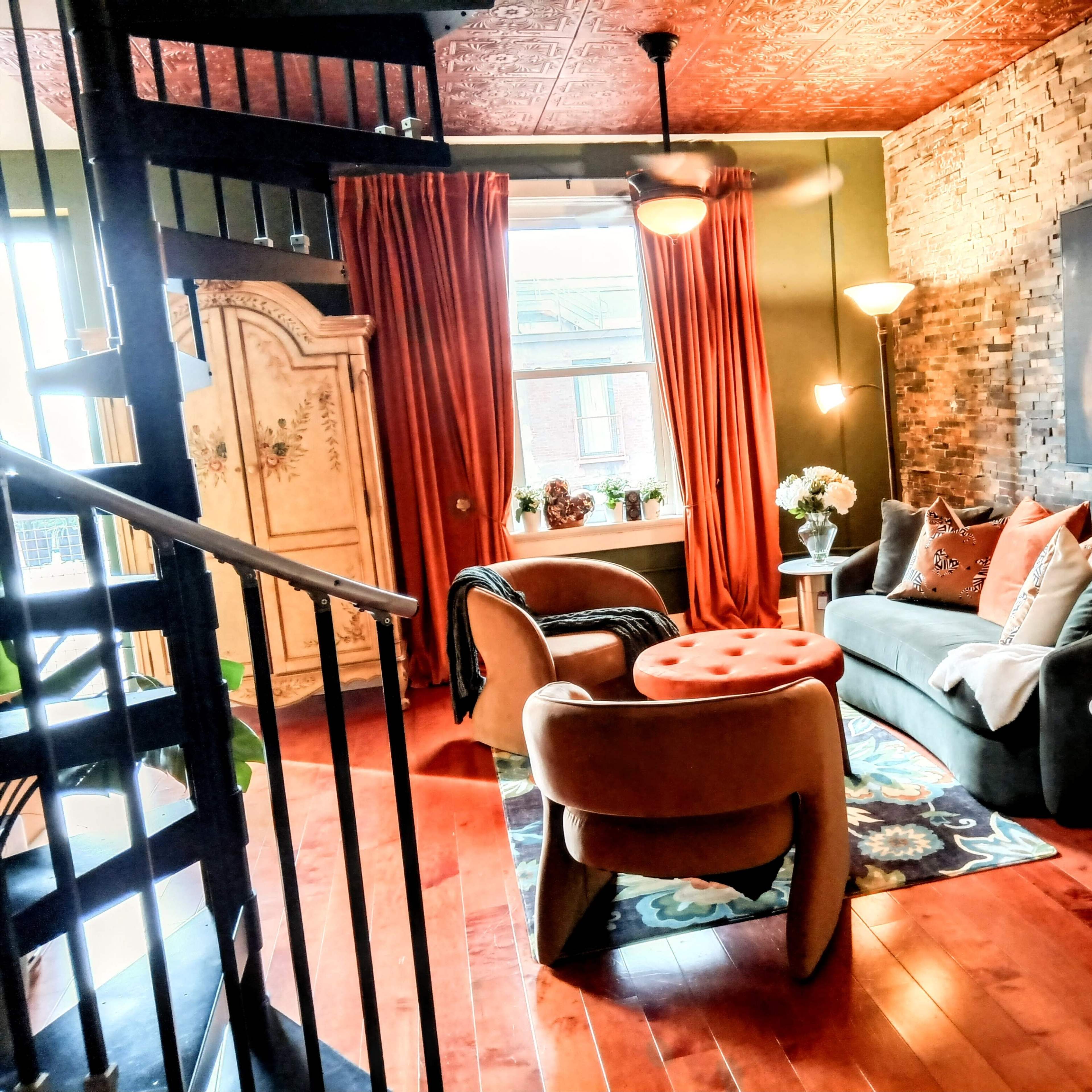 A cozy living room with a spiral staircase, stone-accented walls, large windows, and stylish furniture, including a sofa and a round coffee table.