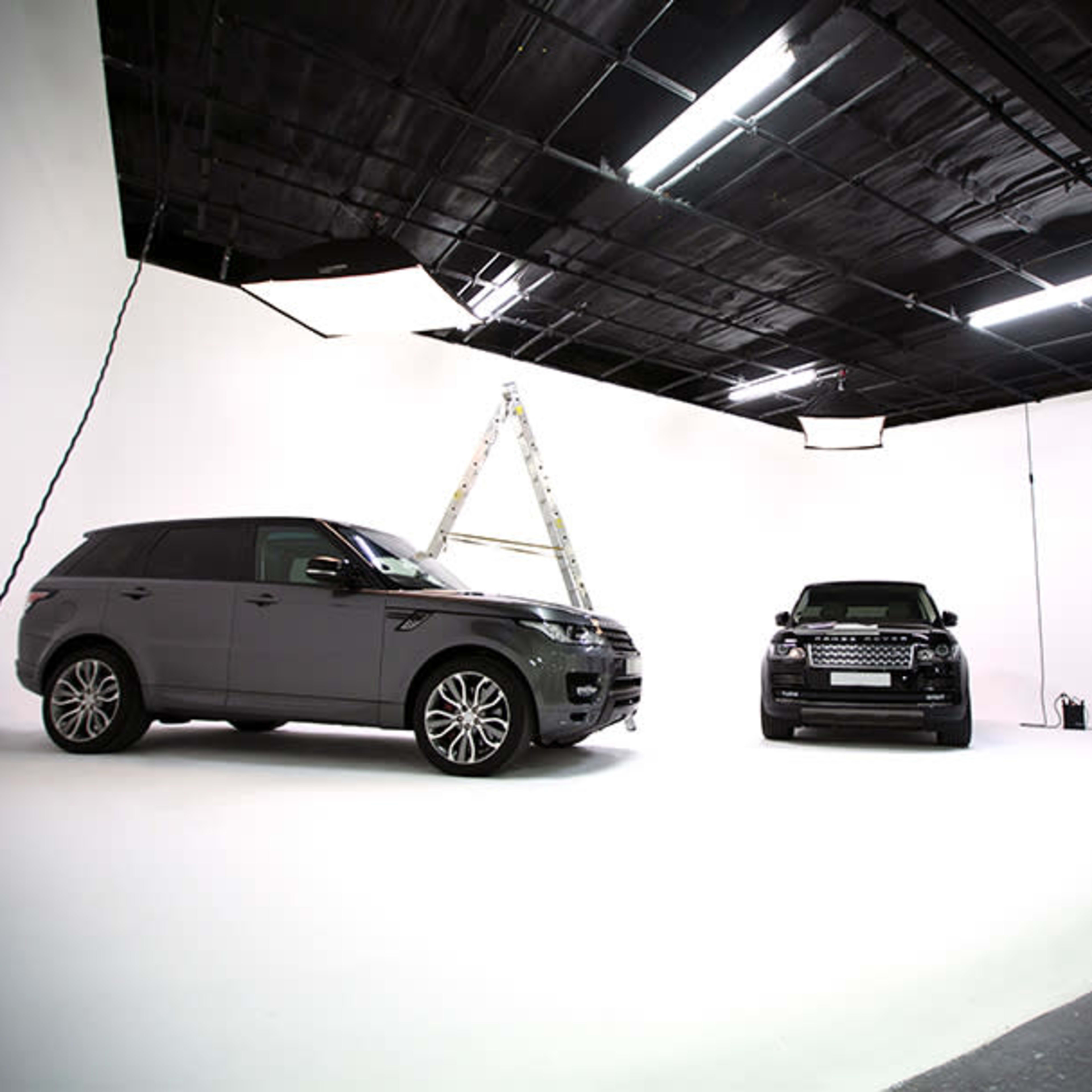 Two luxury SUVs parked in a photography studio with a ladder set up in the background.