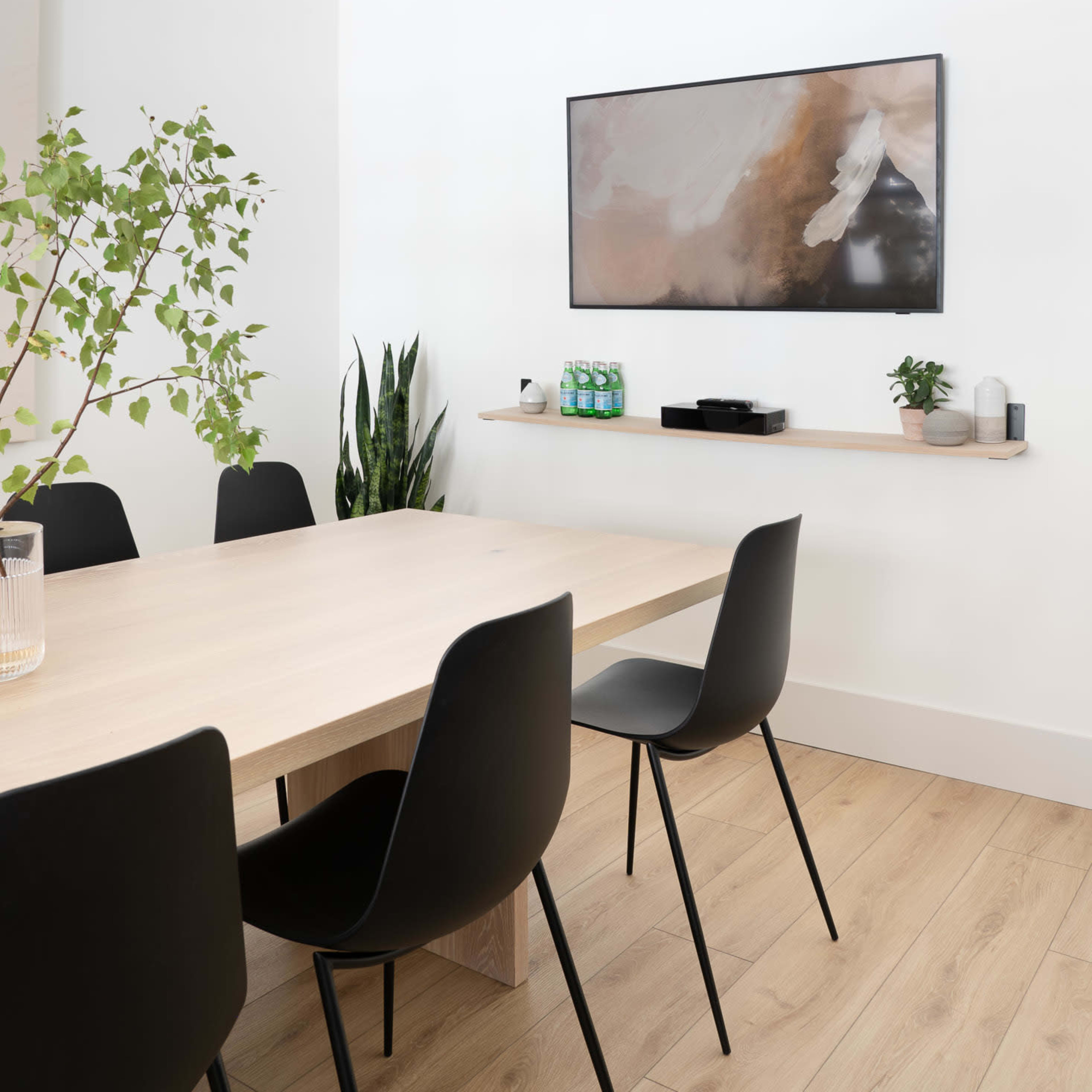 A modern dining area features a wooden table surrounded by black chairs, with a wall-mounted television and minimalist decor.