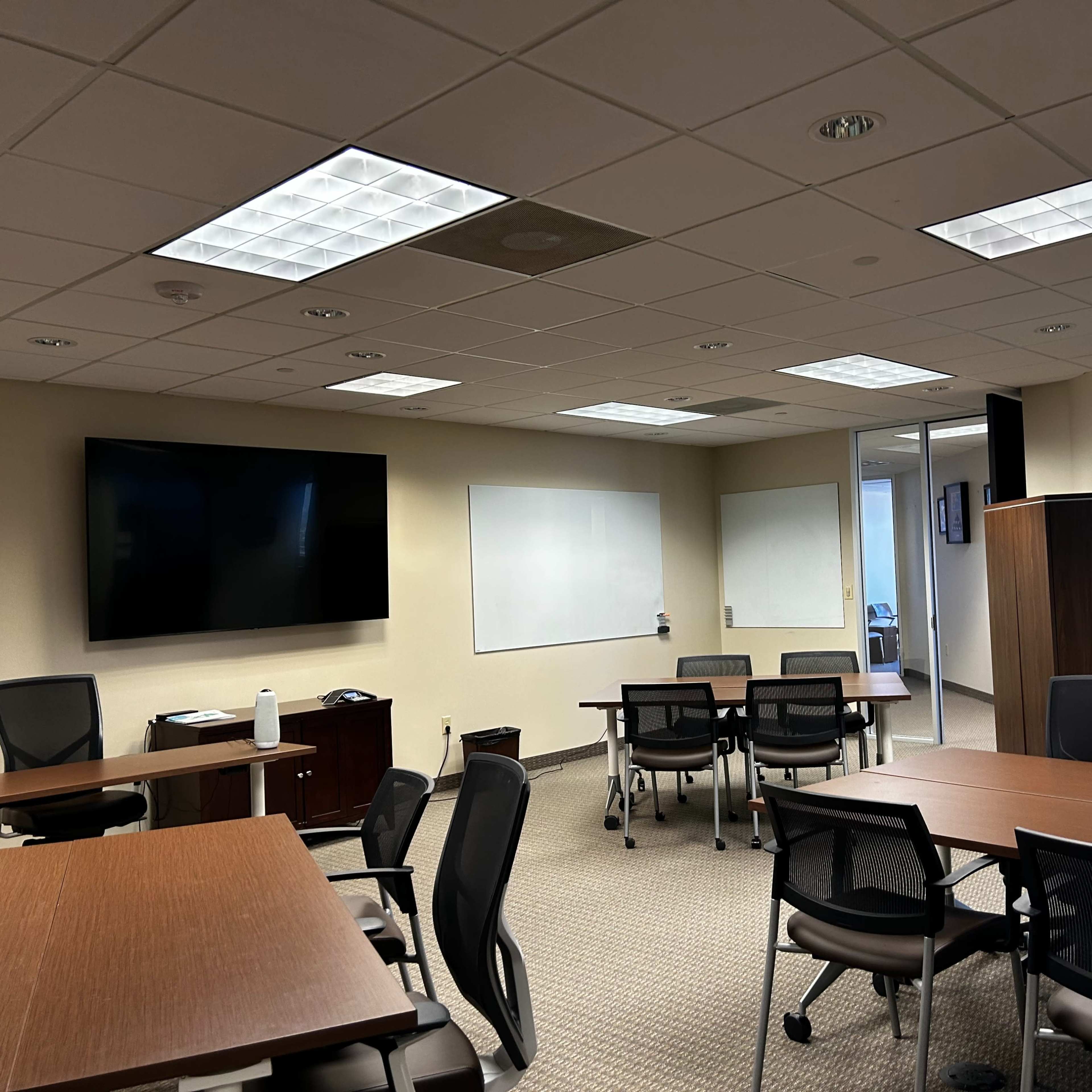 A modern conference room with multiple tables and chairs, a large screen mounted on the wall, and whiteboards for notes.
