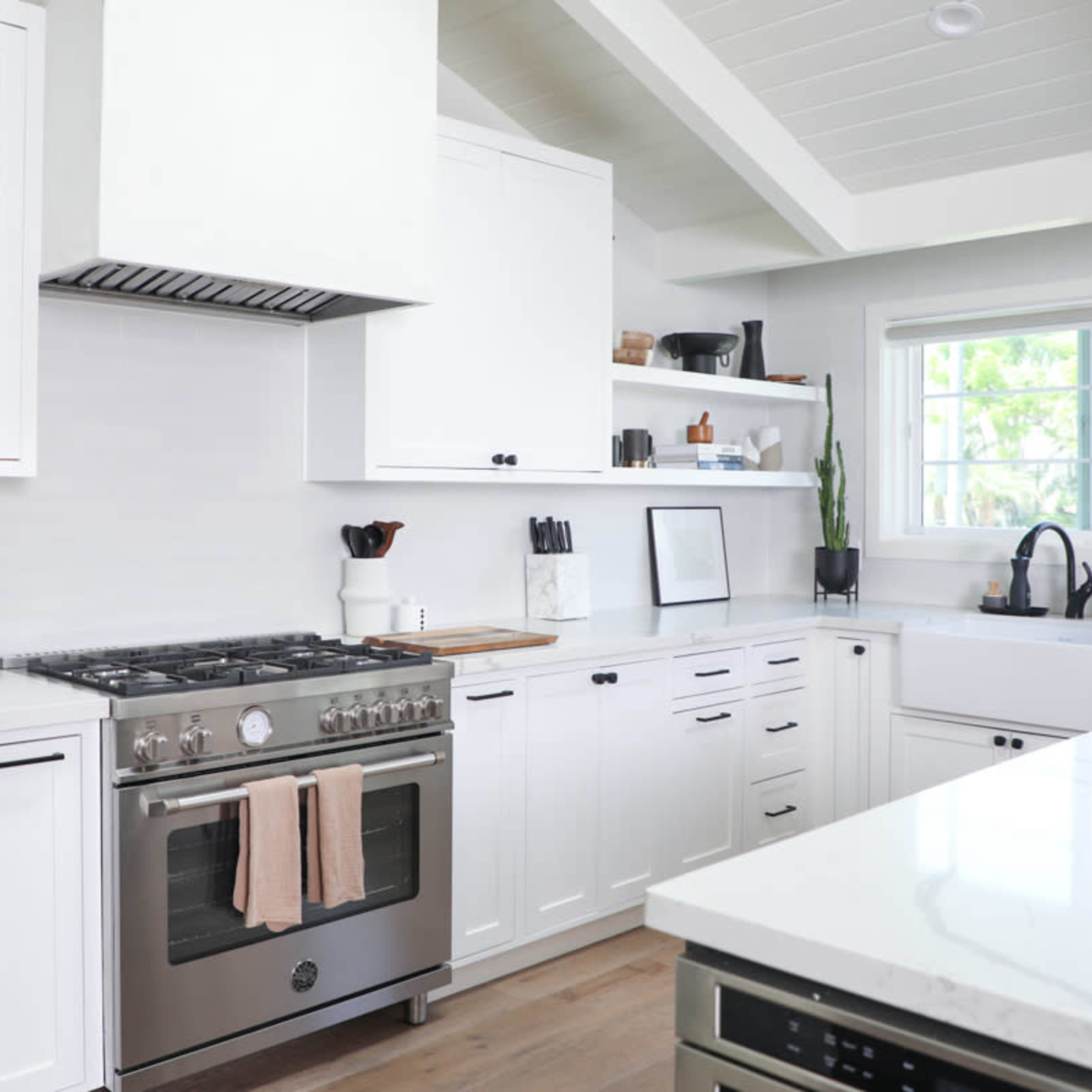 A modern kitchen with white cabinetry, a stainless steel stove, and a large island with a countertop.
