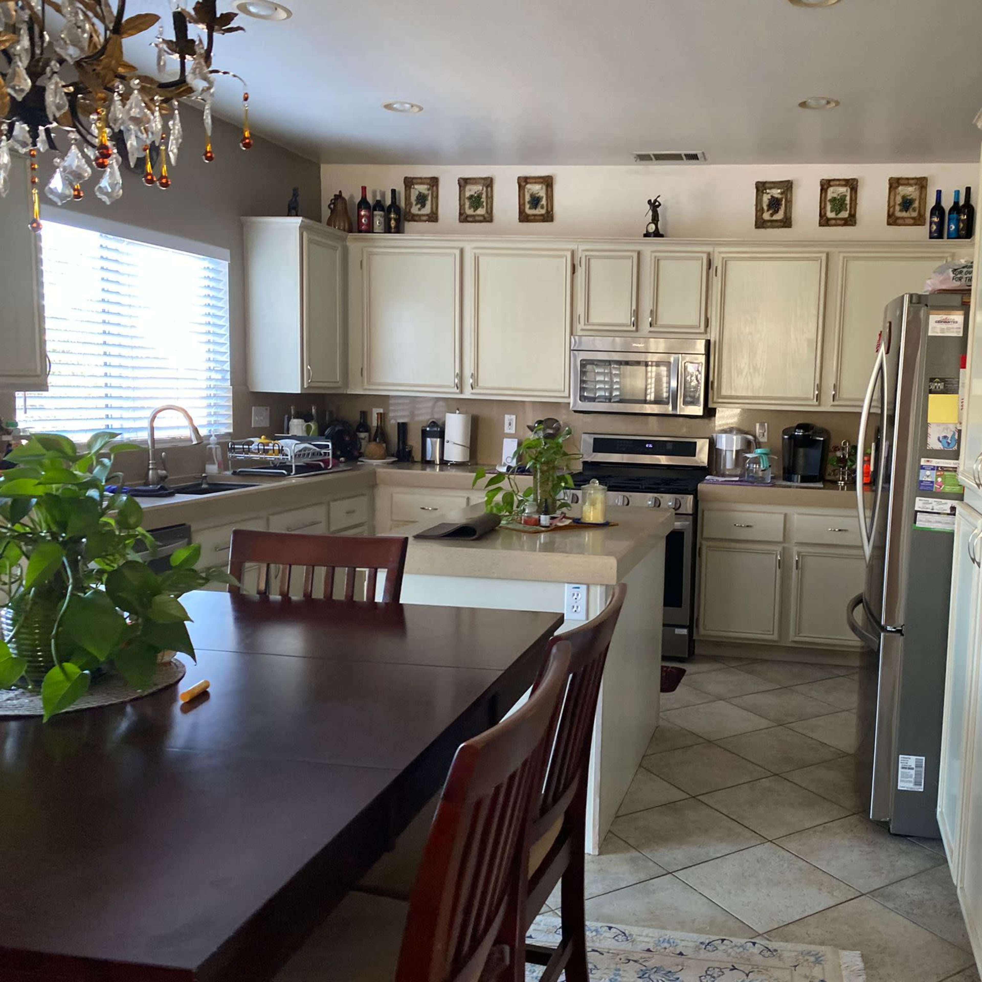 A kitchen with beige cabinets, stainless steel appliances, a dining table, and a window allowing natural light to enter.