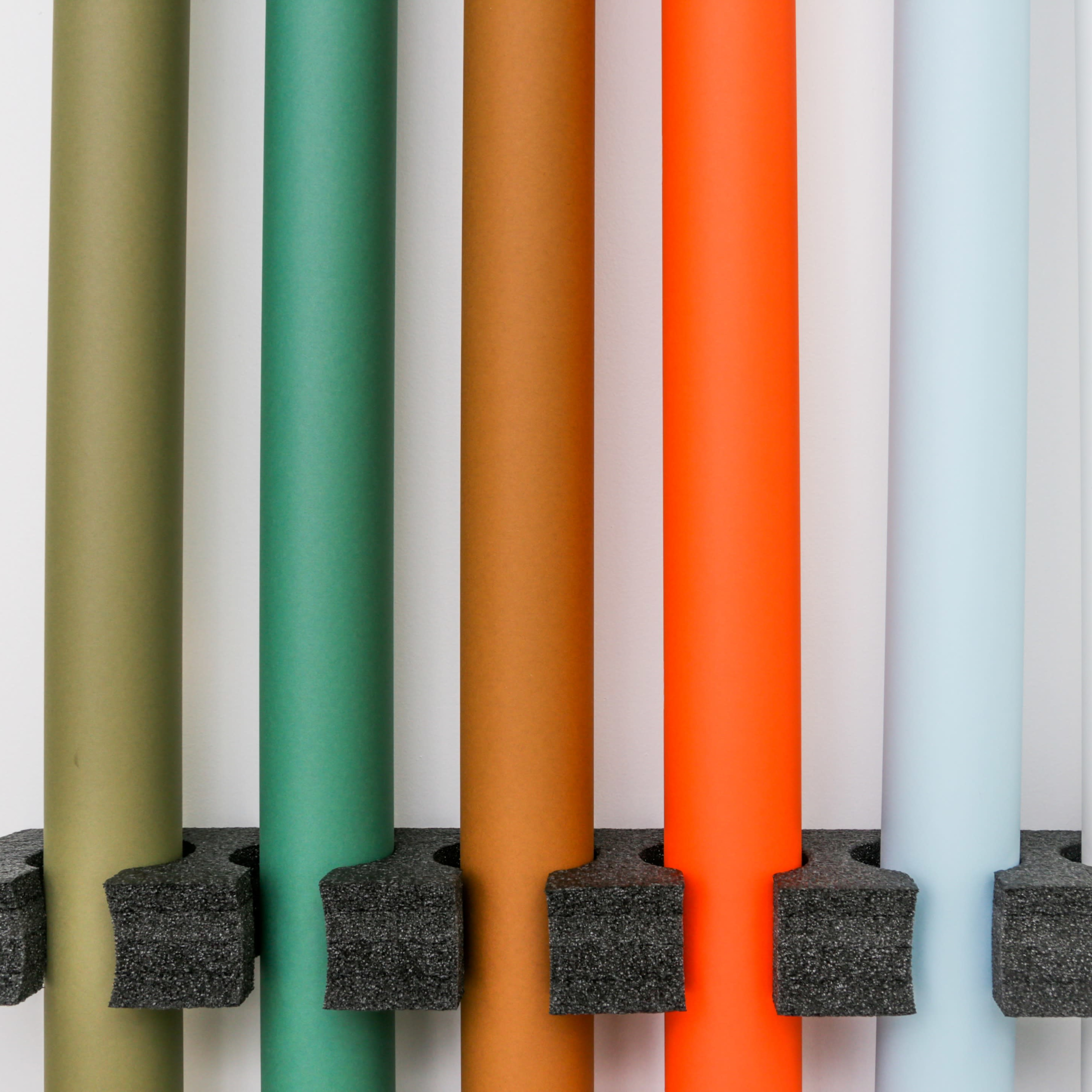 A series of vertically arranged colored paper rolls are mounted on a black holder against a white background.