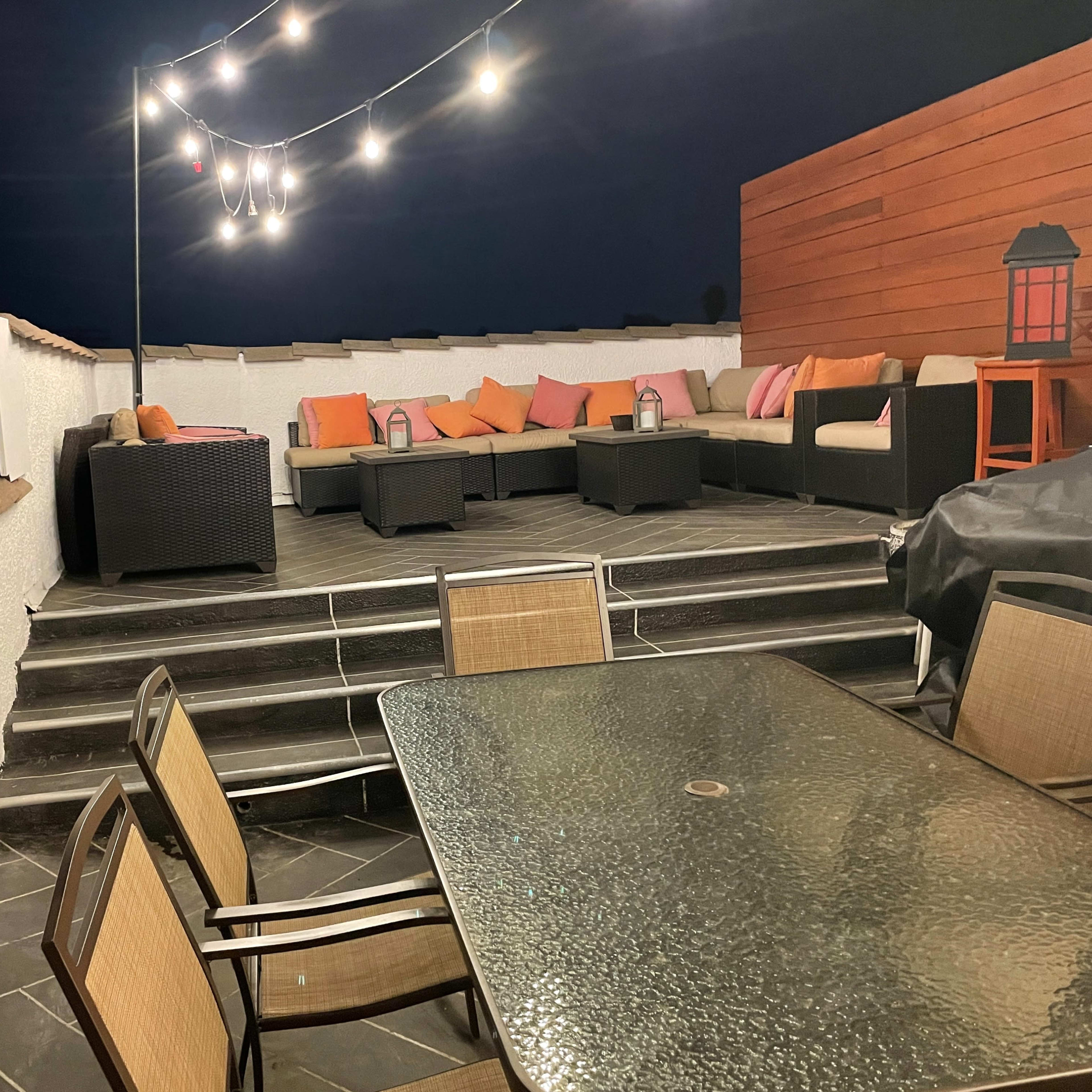 A rooftop terrace area with a sectional sofa, a table, and decorative string lights.